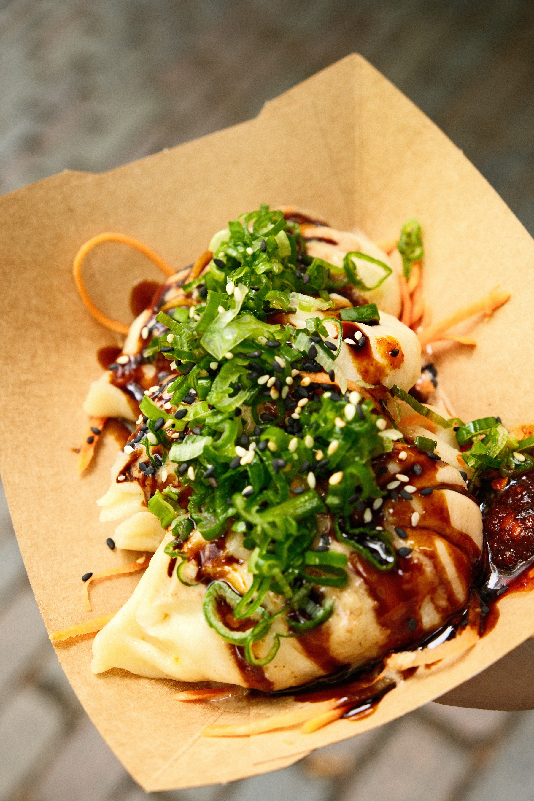 A small basket of half-moon shaped steamed dumplings with various sauces including chili and garnished with chives and thinly sliced carrots