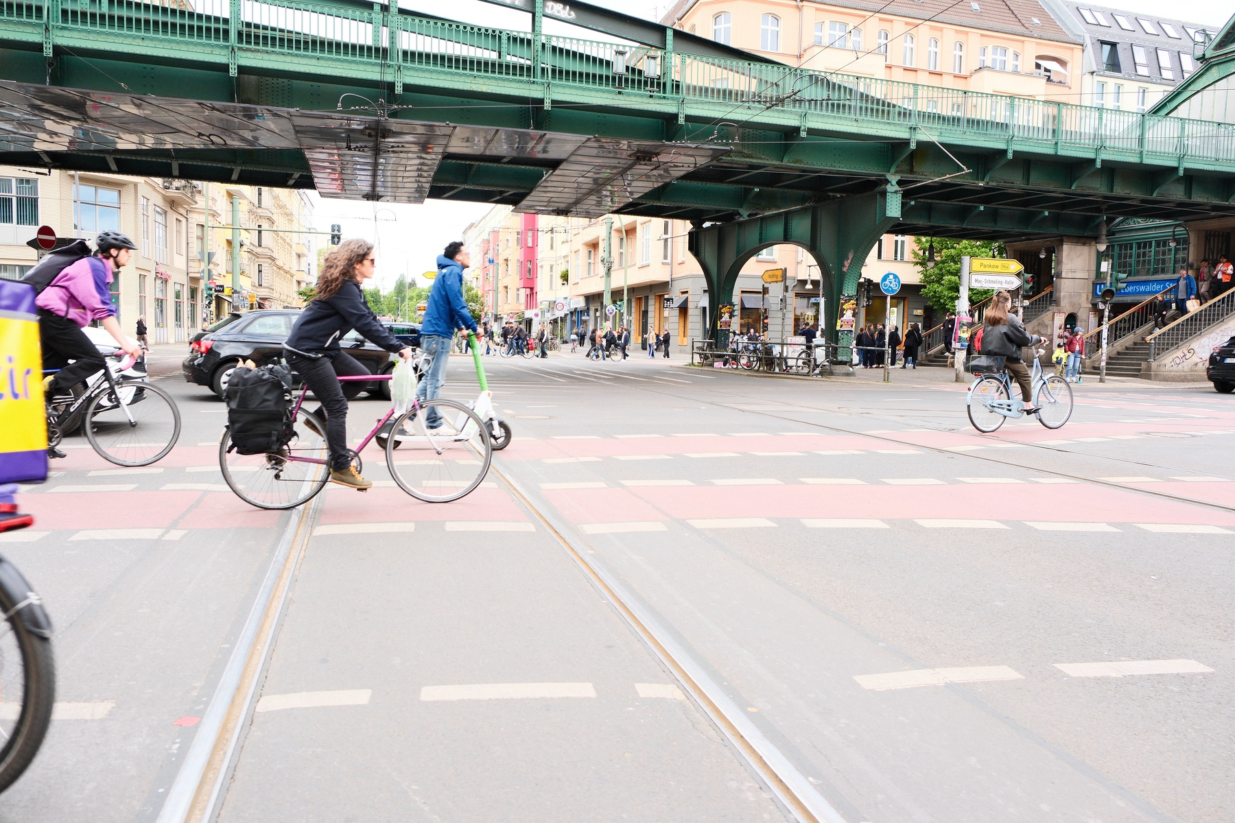 DSCF9959.JPG Many bikes and a scooter cross in painted bike lanes within a wide intersection of Eberswalde Strasse, Danziger Strasse, Shönnhauser Allee, and Pappalalle near the Kulturbraurei. A green overcrossing for the U-bahn(?) crosses over.