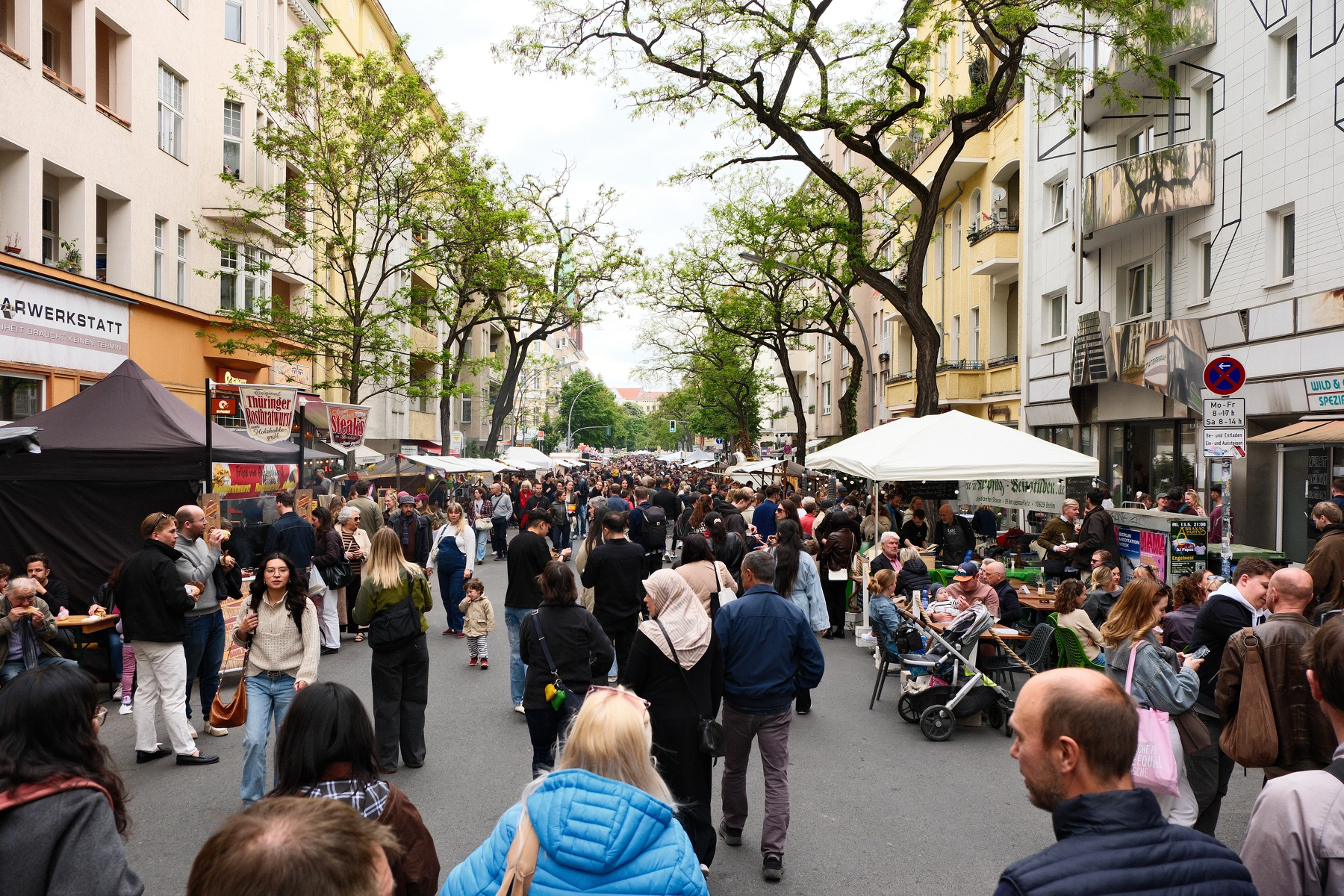 DSCF9989.JPG A street filled with people walking at the Spargelfest with many vendors under canopies along the sides of the streets. The street is surrounded by multistory buildings and bendy-trees.