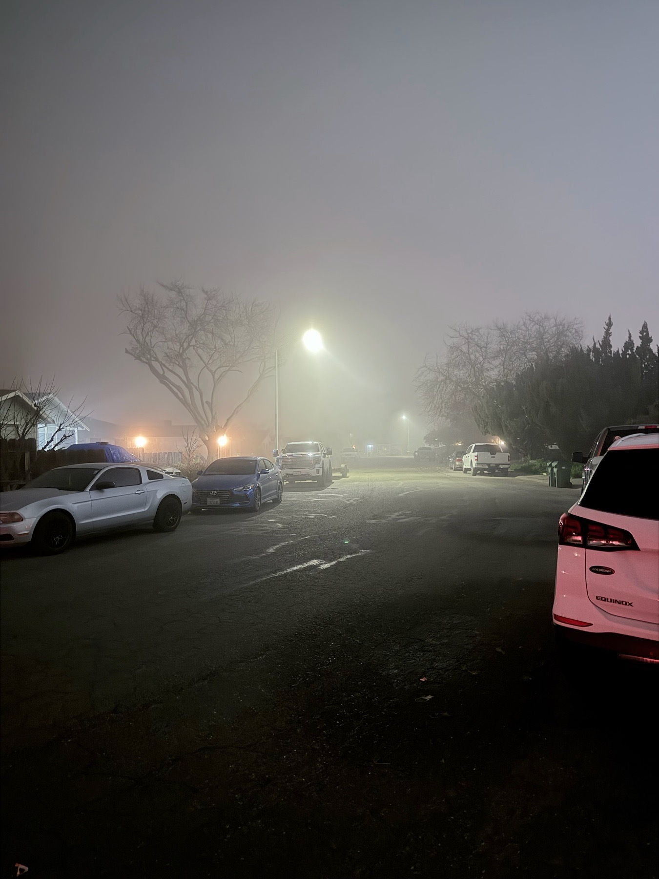 A foggy residential neighborhood with about a quarter mile visibility. The end of the street is barely visible about 5 houses down. 