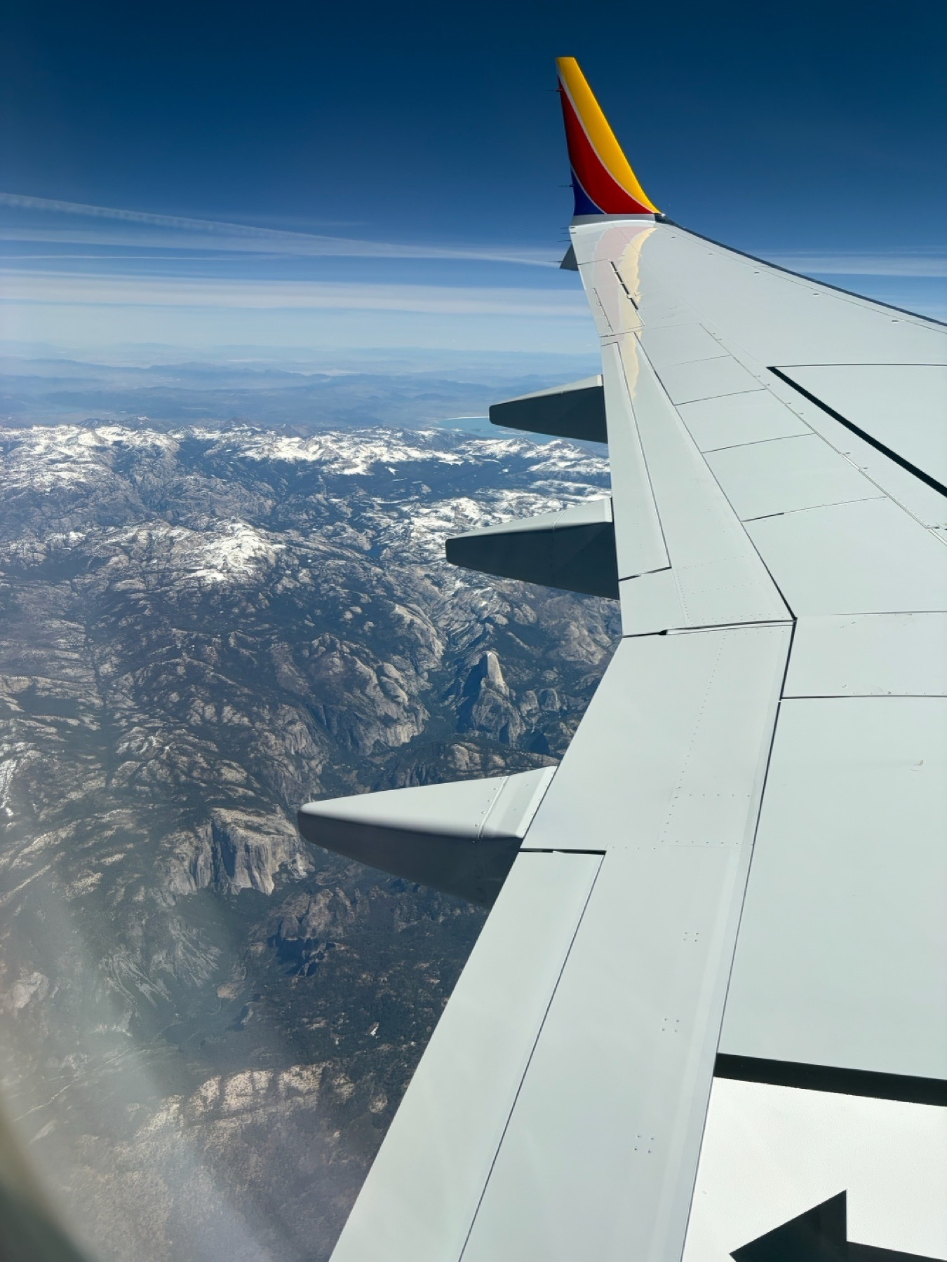 A view out a left passenger windup with a view of a 737 Max wing with Southwest style winglets. It’s a mostly clear sky with Yosemite below where the Sierra Creat still has some snow and Half Dome rises prominently over the green & snowless U-shaped Yosemite Valley