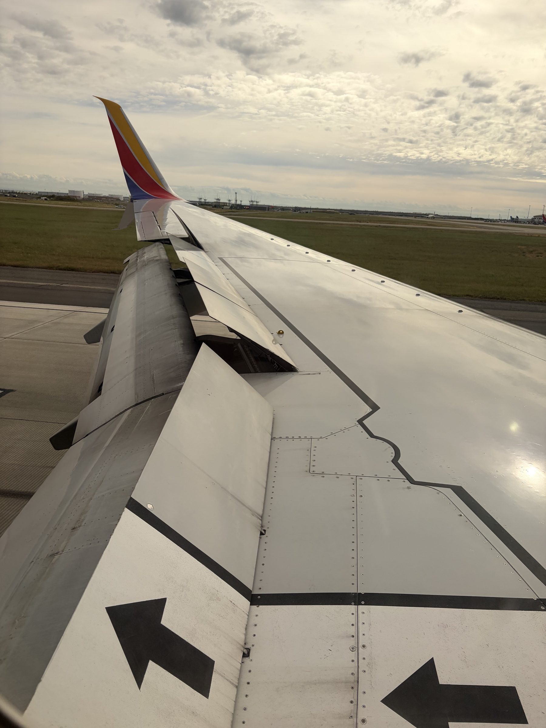 IMG_0338.jpeg An over wing view of a Southwest B737-700 landing at Sacramento International on an overcast day. The speed brakes are about half deployed while the flaps are around 30 degrees. Arrows near the window point the way off the jet during an emergency.