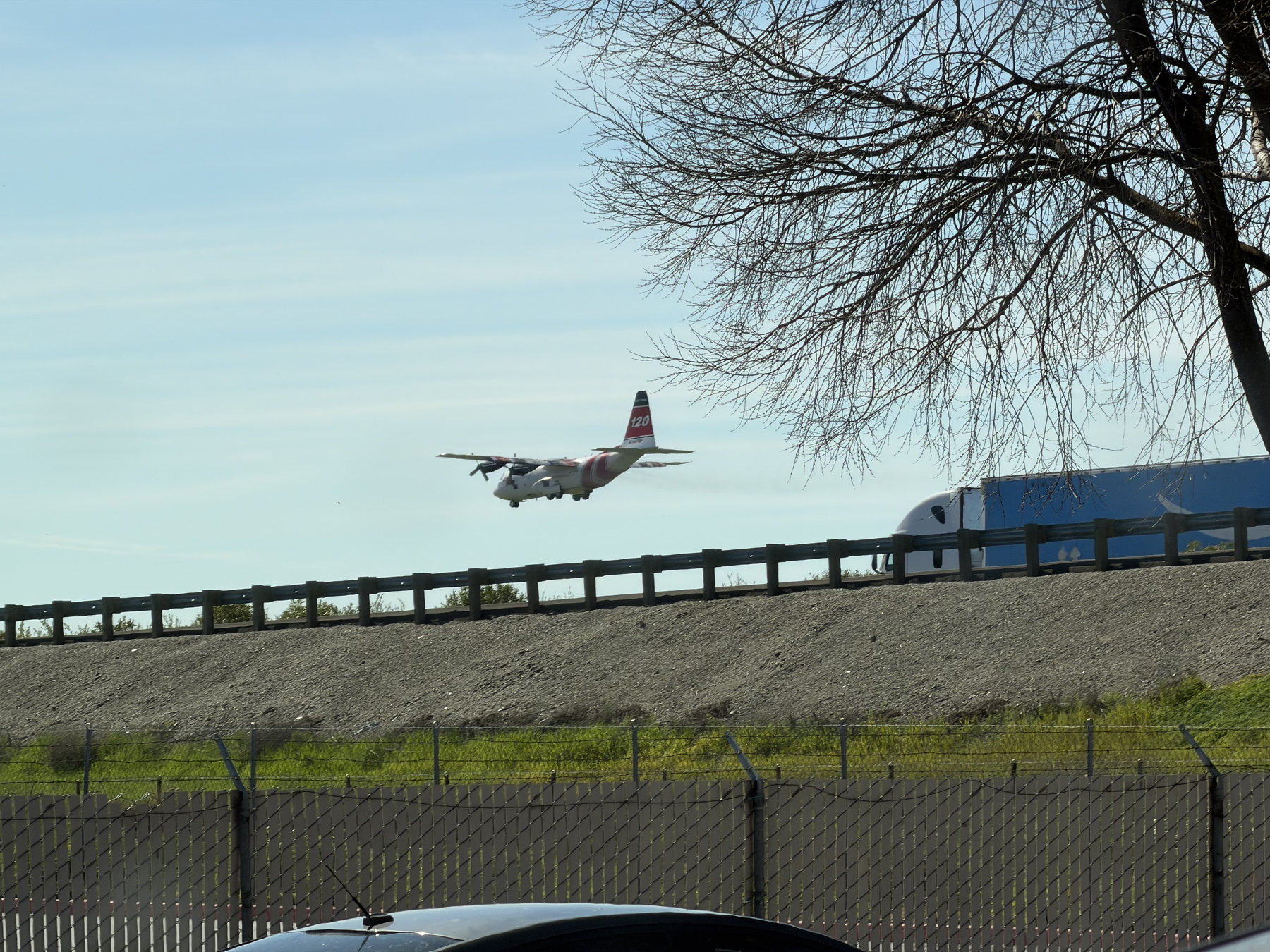 IMG_0729.jpeg A C130 on approach to Willows Airport, just above the giant berm of I-5, the airport hidden behind that berm. Its red tail has a 120 on it and two of its turboprop engines can be seen. Its gear is down.