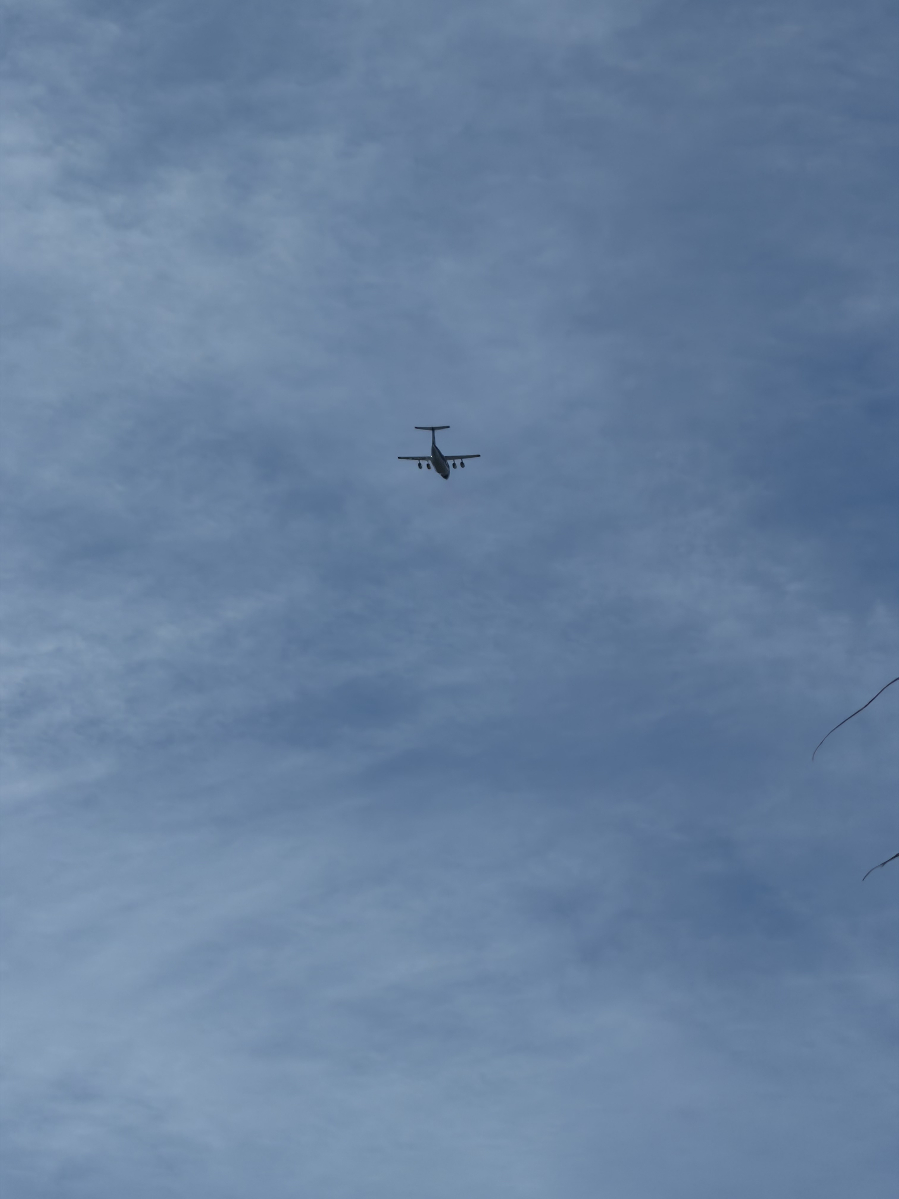 IMG_0750.jpeg An silohette of a Aero-Flite RJ85 flies overhead against a blue sky with thin, somewhat chaotic and translucent clouds. It's a bit off in the distance but its four engines and T tail are clearly visible.