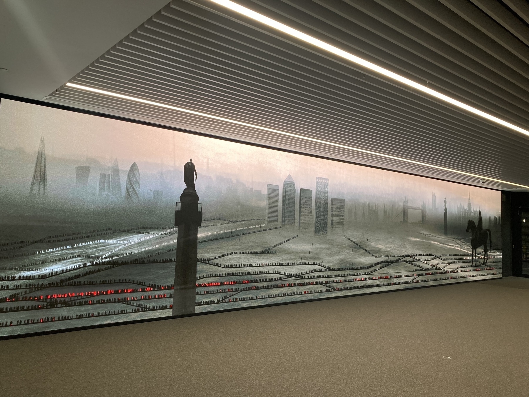 Photo of a screen-based art exhibit at Crossrail Place, London that shows a dramatic, imaginary Londonscape with moving figures above and below ground