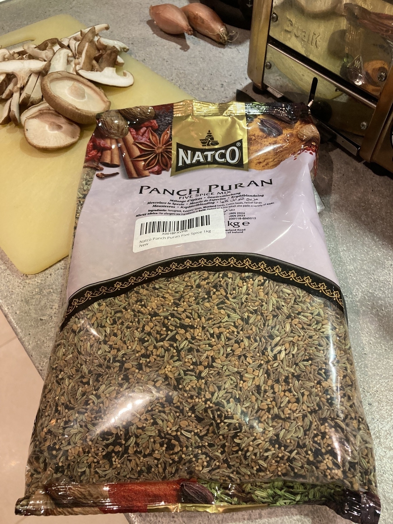 A large pack of Bengali 5 Spice on a chopping board with mushrooms.