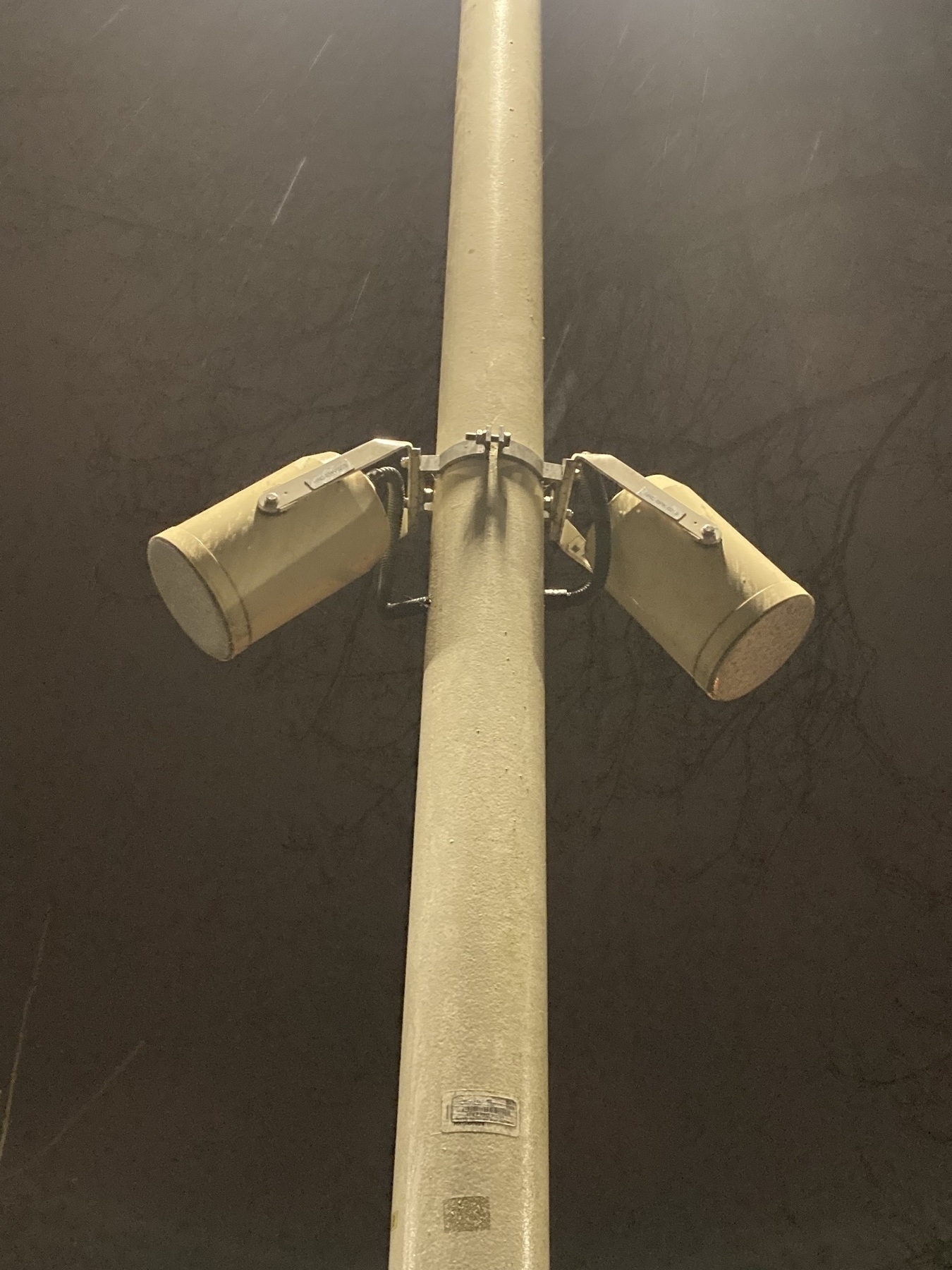 Paired cylindrical public address speakers on a lampost in the rain