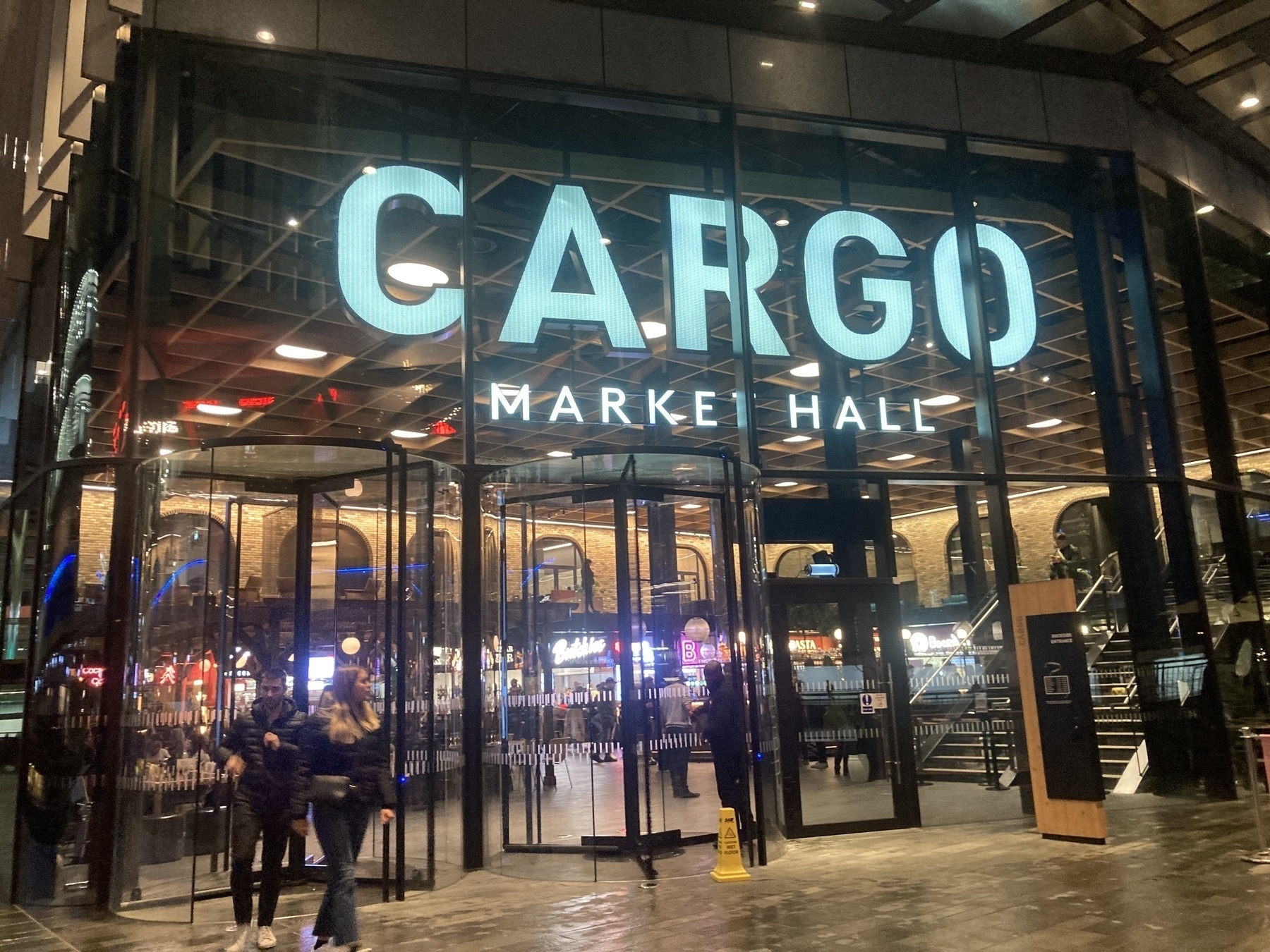 A couple leave the Cargo Market Hall food court in Canary Wharf on a wet spring evening