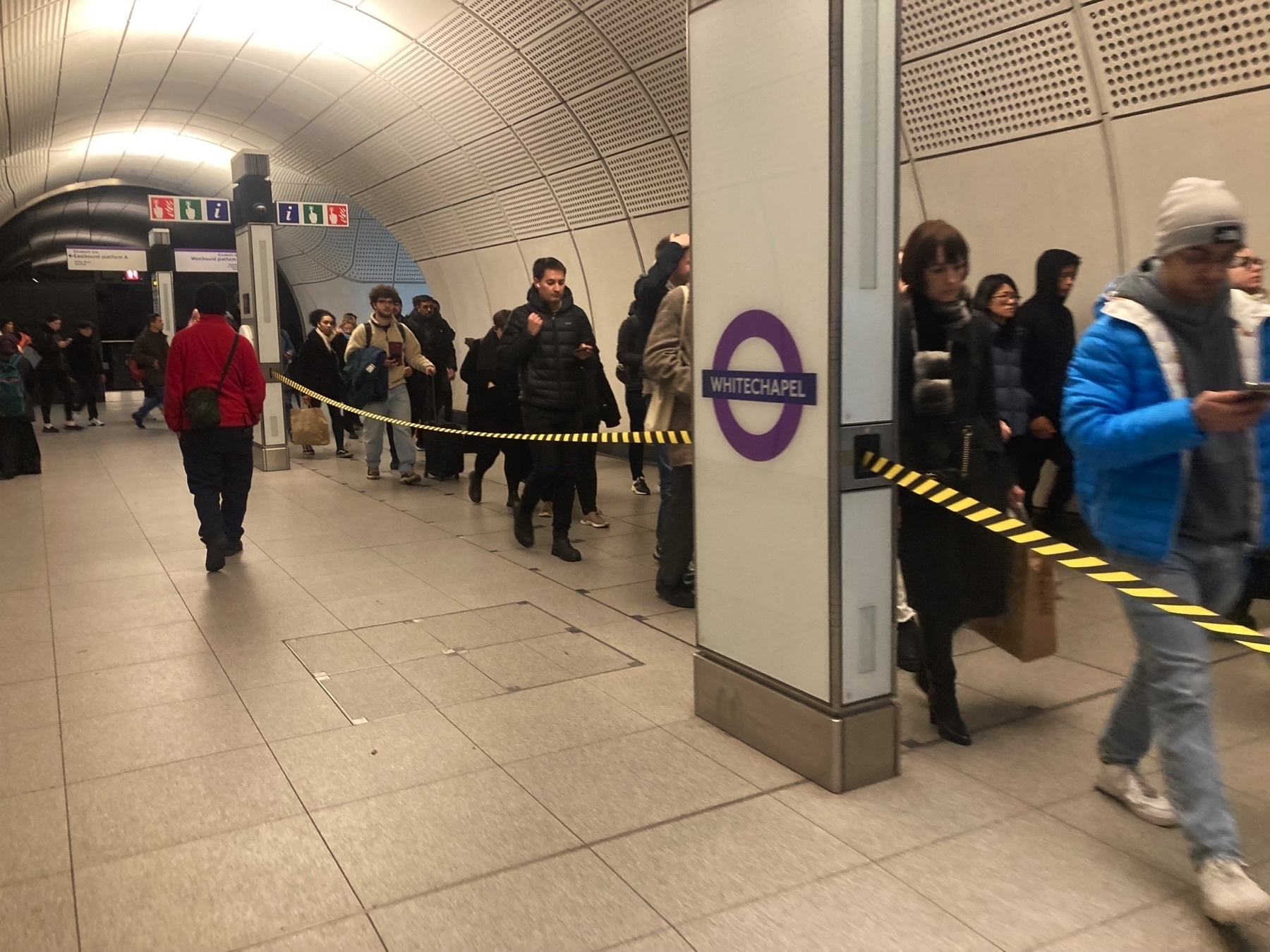 Passengers separated by a tape barrier for crowd control on the Elizabeth Line in Whitechapel, East London