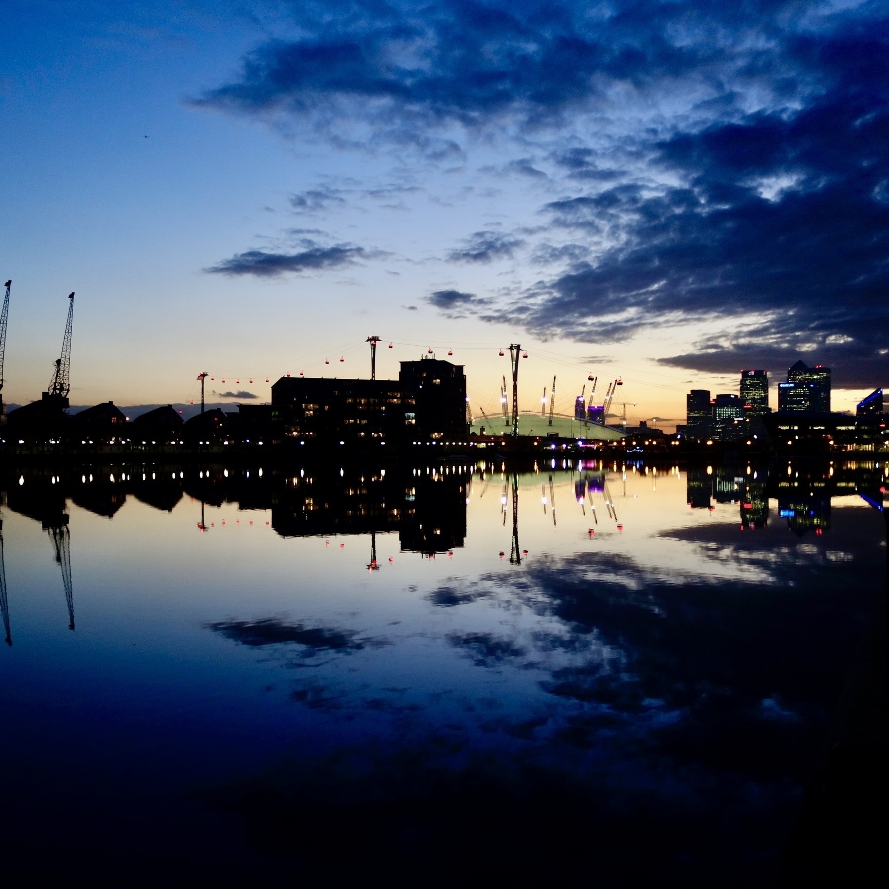 Dusk at the Royal Docks in East London, light fading from blue to yellow at the horizon, and buildings reflected in the water