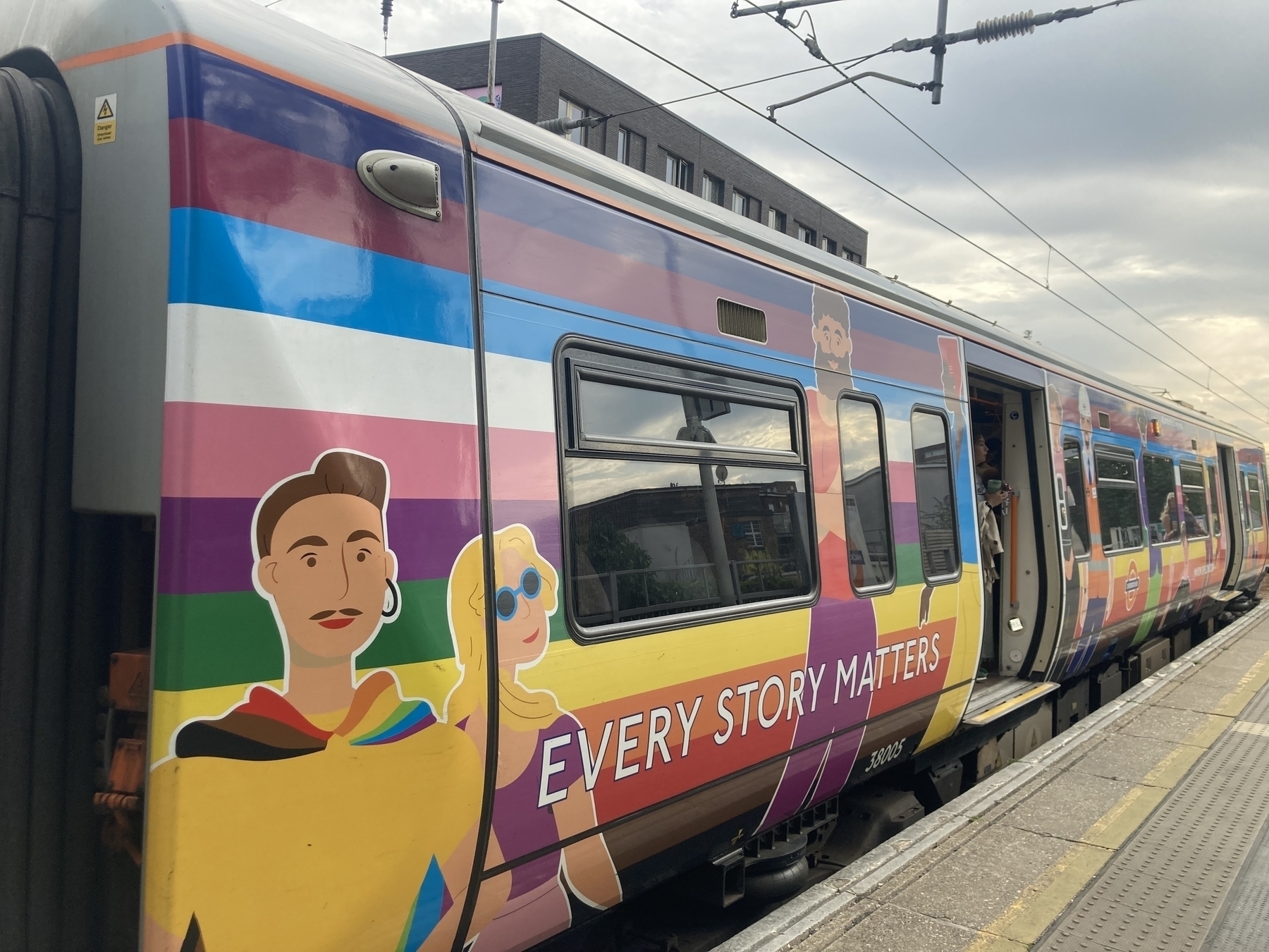 Commuter train at a station platform. It is painted in rainbow colours to celebrate Pride. 