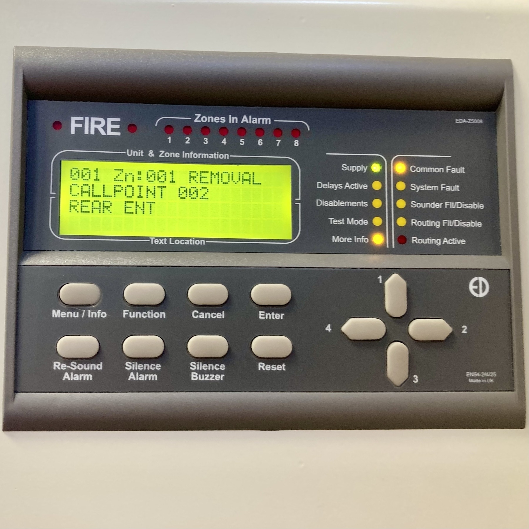 The green illuminated LCD display of a fire alarm panel shows a fault