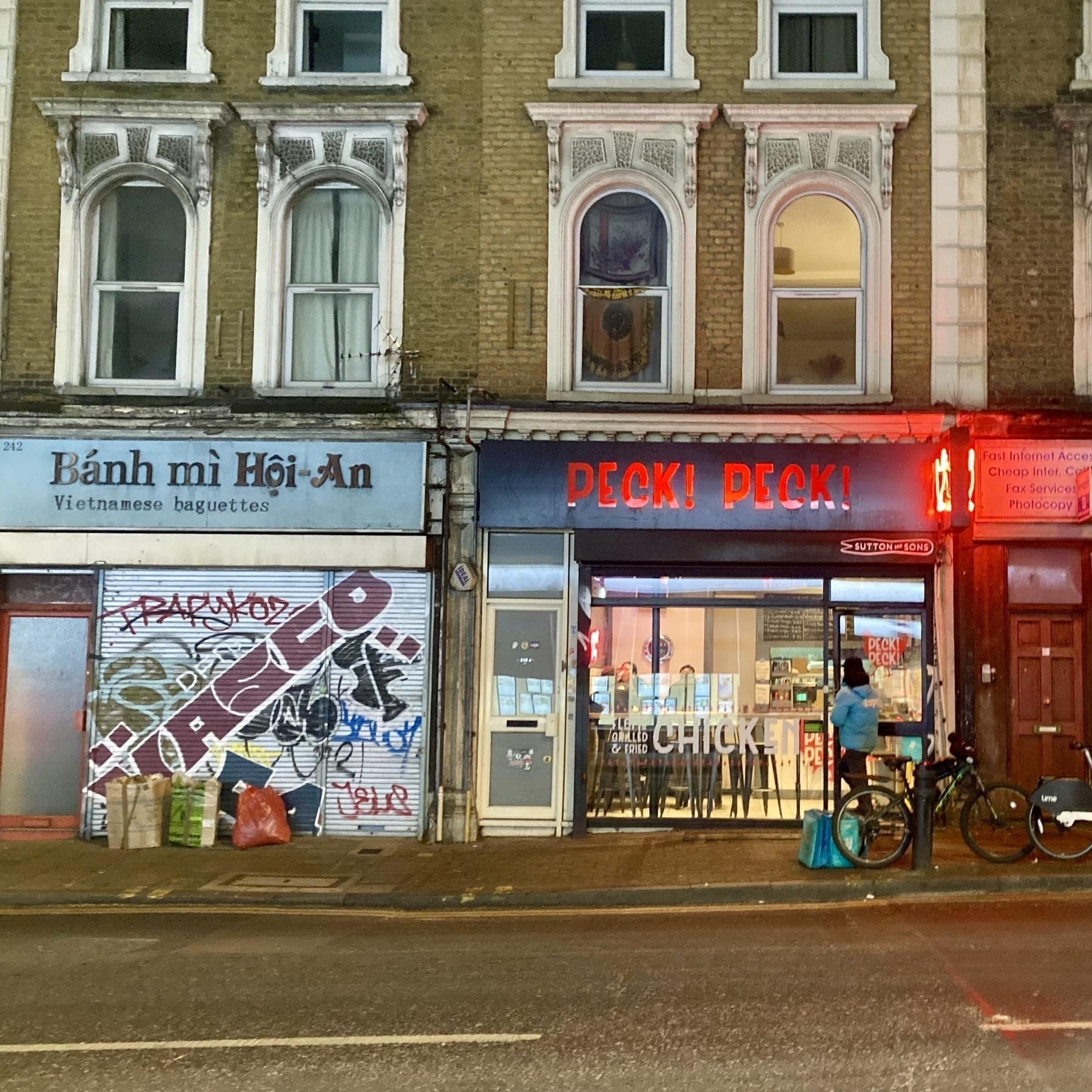 Two takeaway food shops on a Victorian street in East London with rental e-bike in front and a food delivery rider.