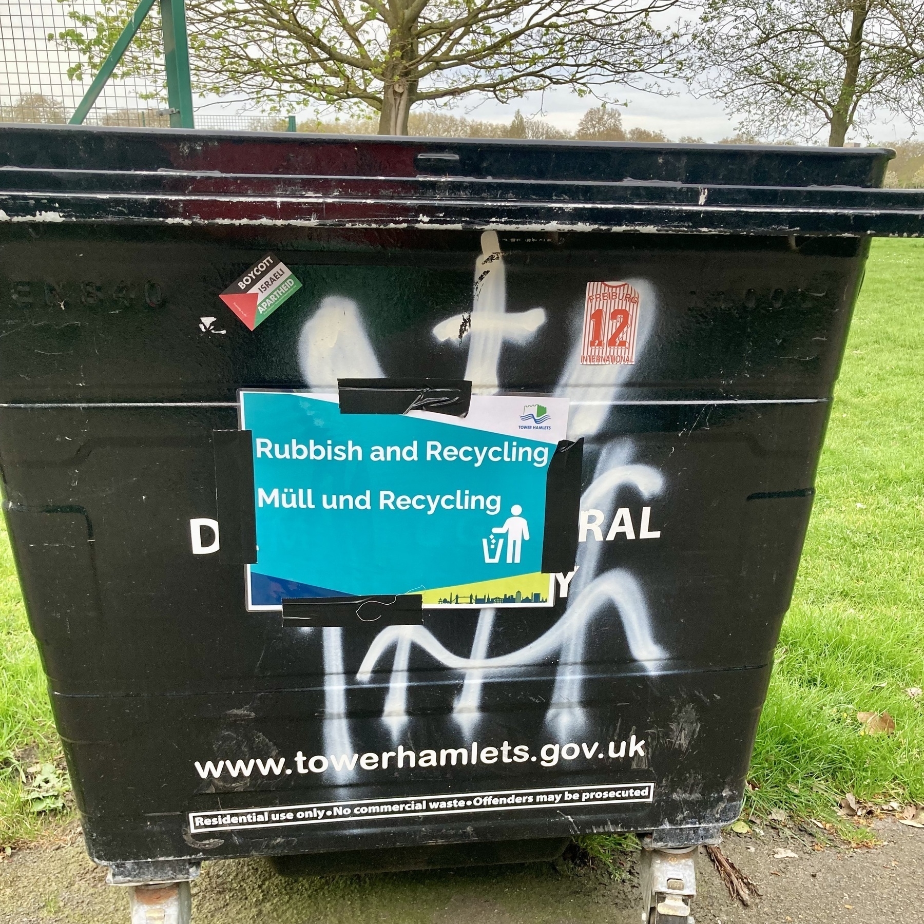 A black dumpster with a multilingual notice in English and German, and a Free Palestine sticker
