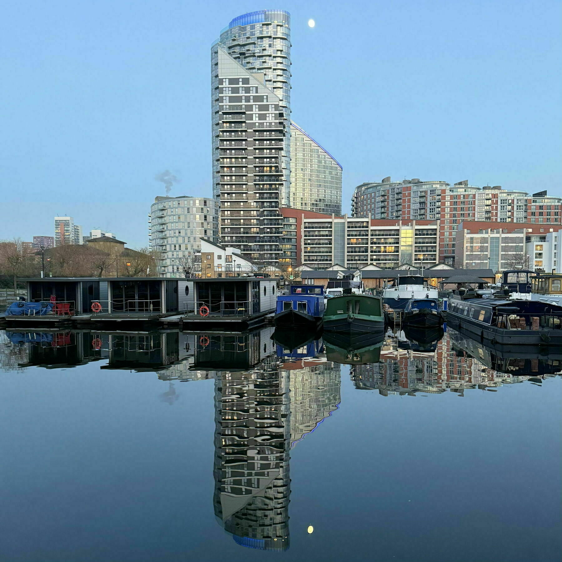 The moon in the east over high-rise buildings, and reflected in the water of Poplar Marina