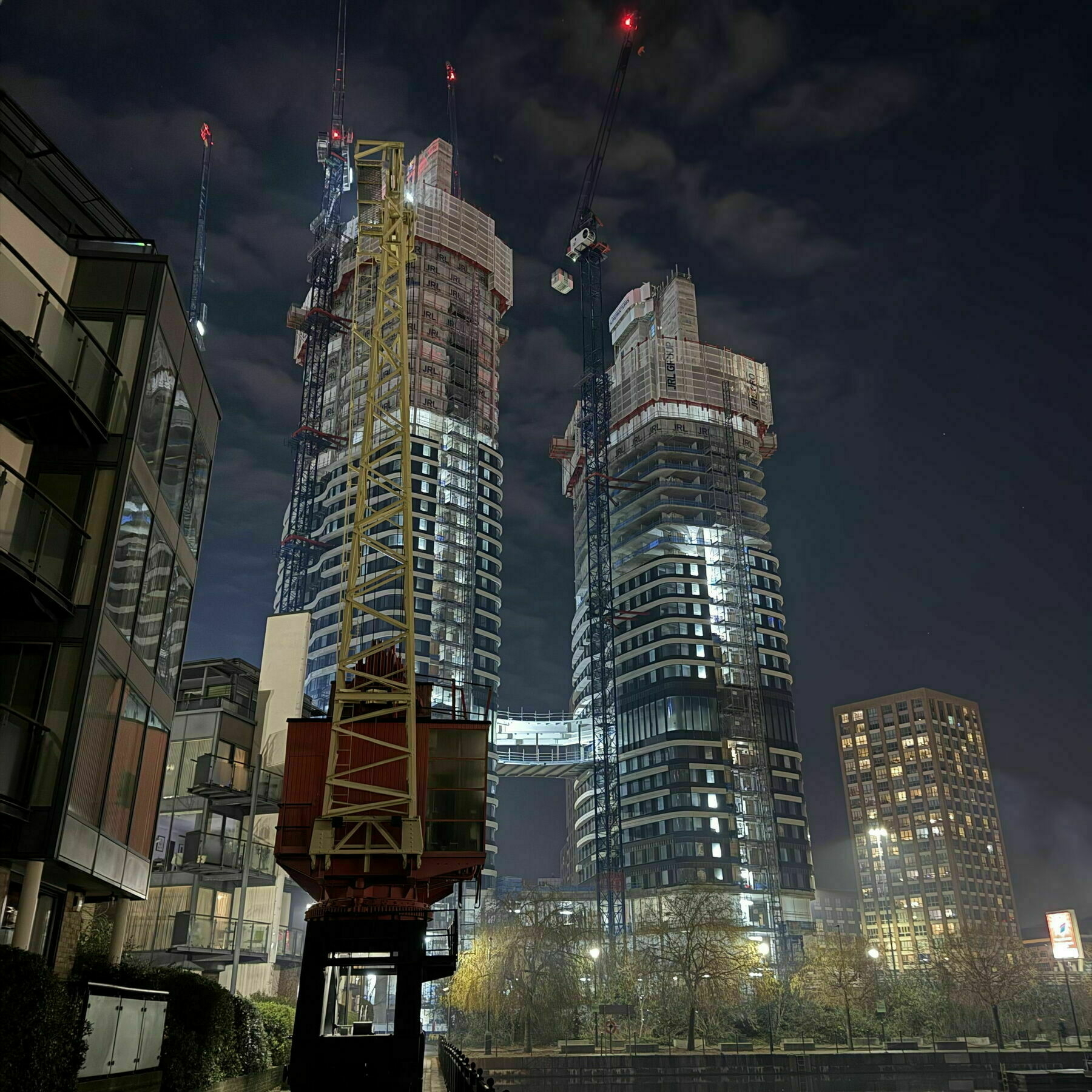 Two half-built residential towers loom over a night-time Poplar Marina