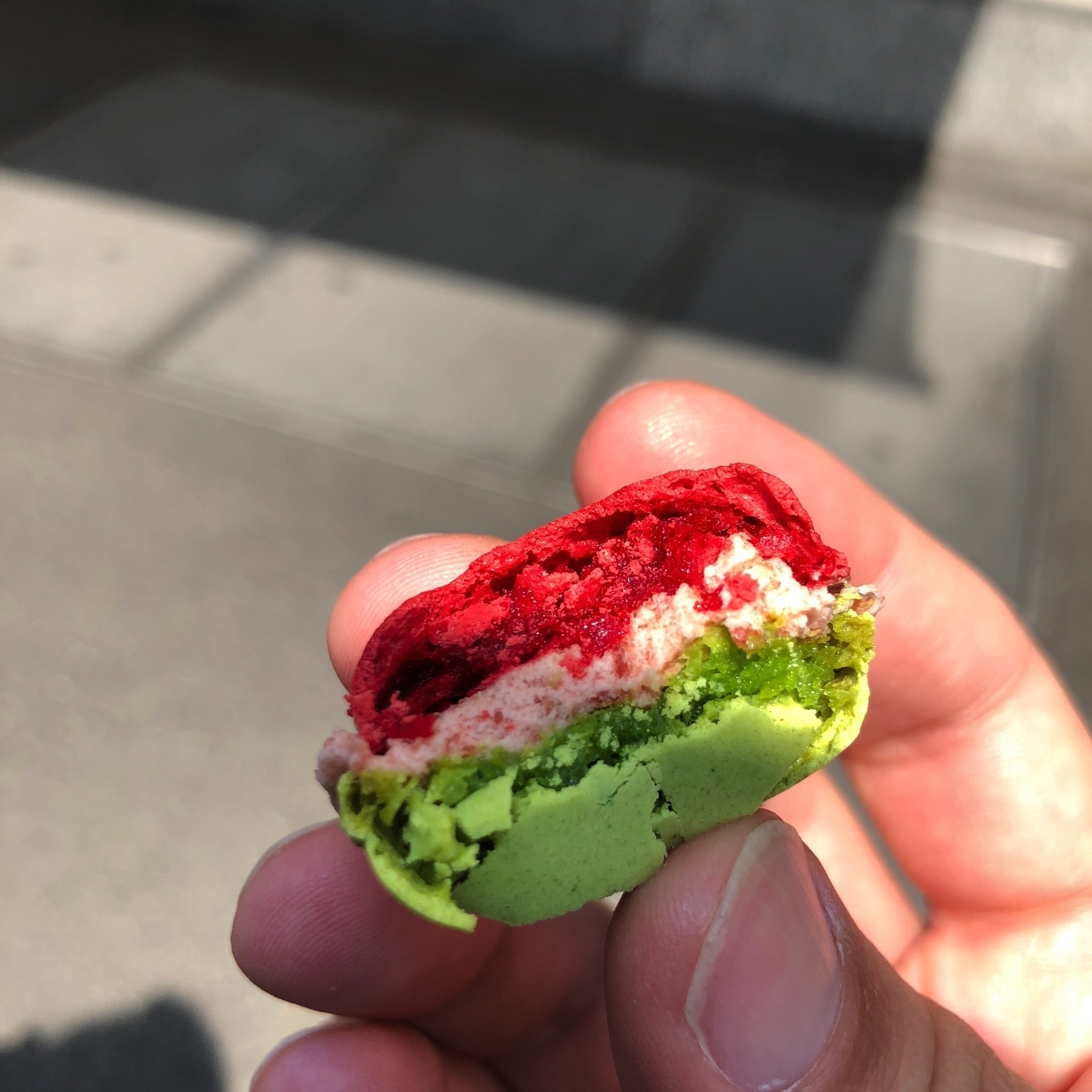 Photo of a bright red and green Luxemburgerli with white filling, with a bite taken out of it.