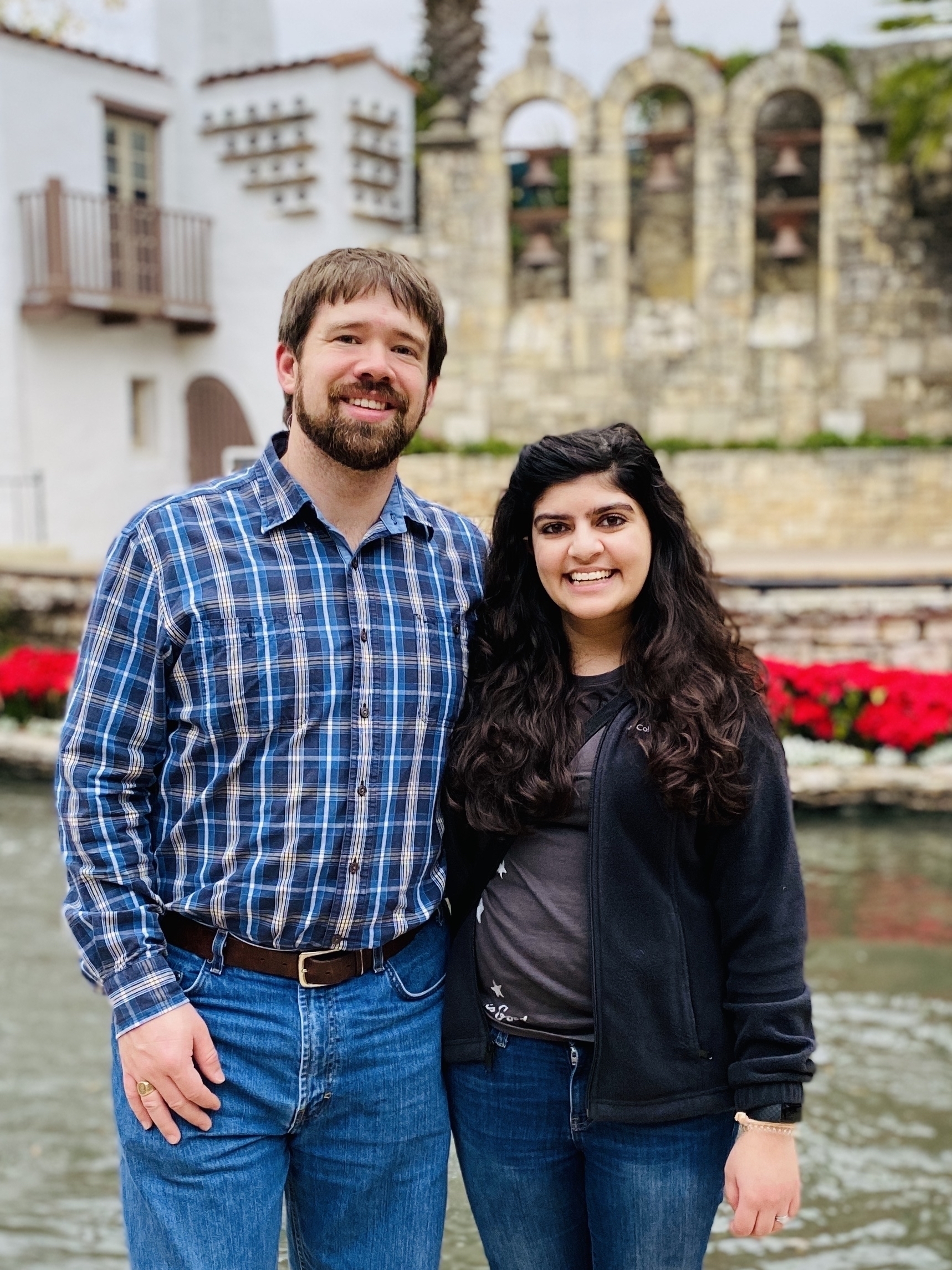 Portrait-mode photo of me and Meera in front of poinsettias and the San Antonio river.