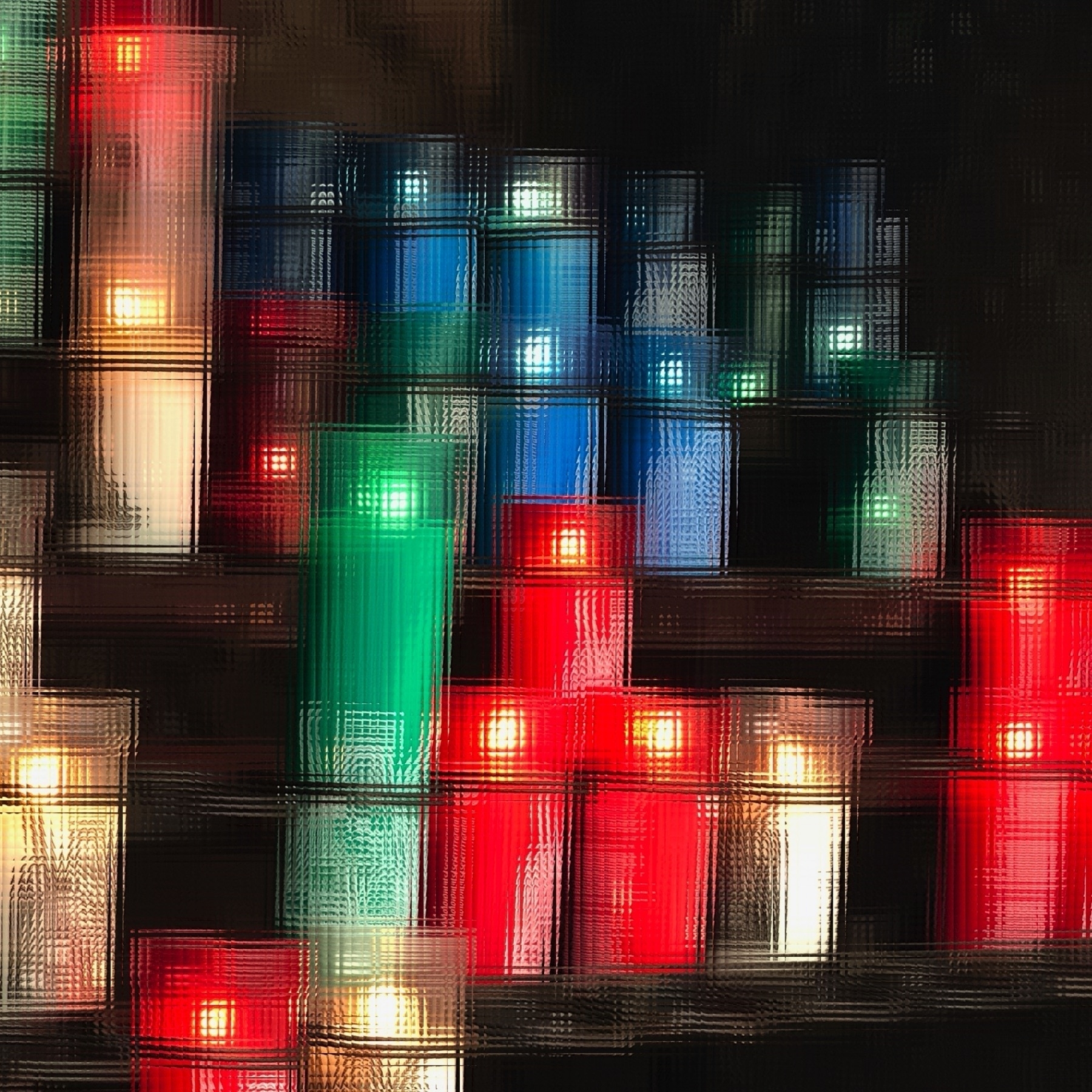 Lit candles on an altar in bright white, red, green, and blue. Stylized like looking through faceted glass.