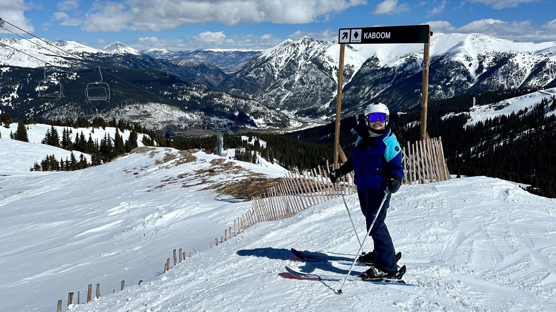 Meera on skis on top of Copper Mountain in front of the sign for the KABOOM black diamond run.