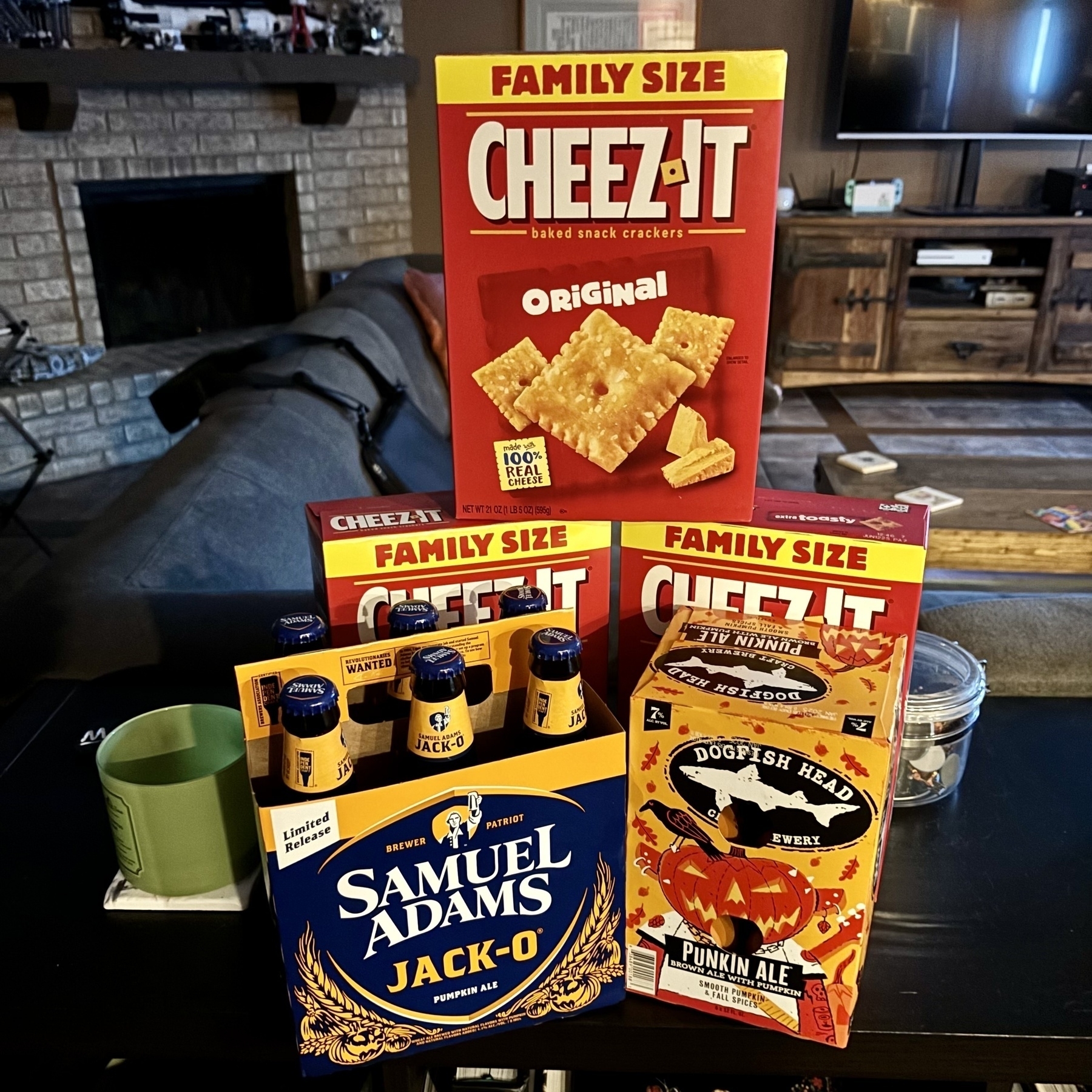 A stack of three family-size boxes of Cheez-Its, a six-pack of Sam Adams Jack-O beer, and a six-pack of Dogfish Head Punkin Ale.