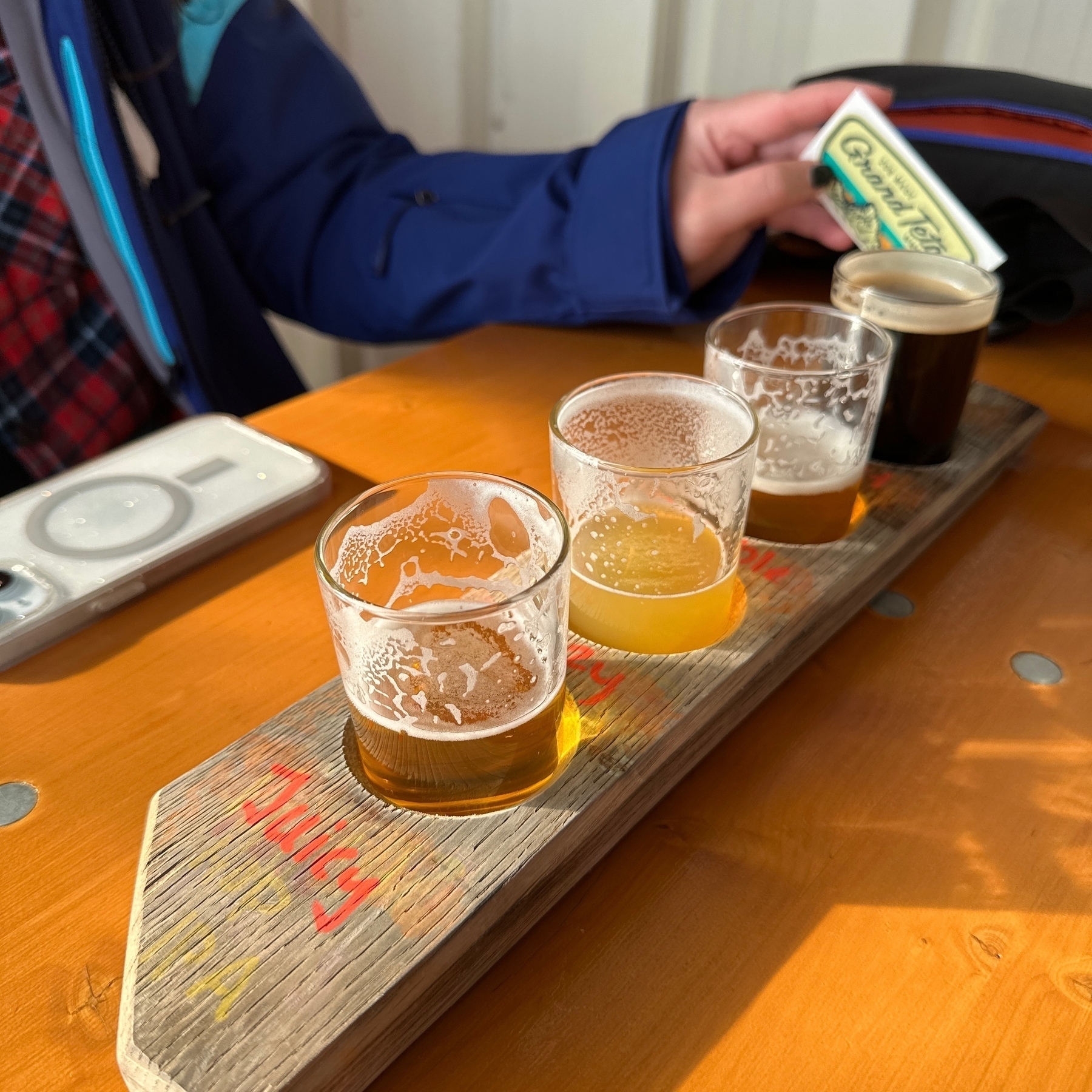 A wooden stave holding four tasting glasses half-full of beers.