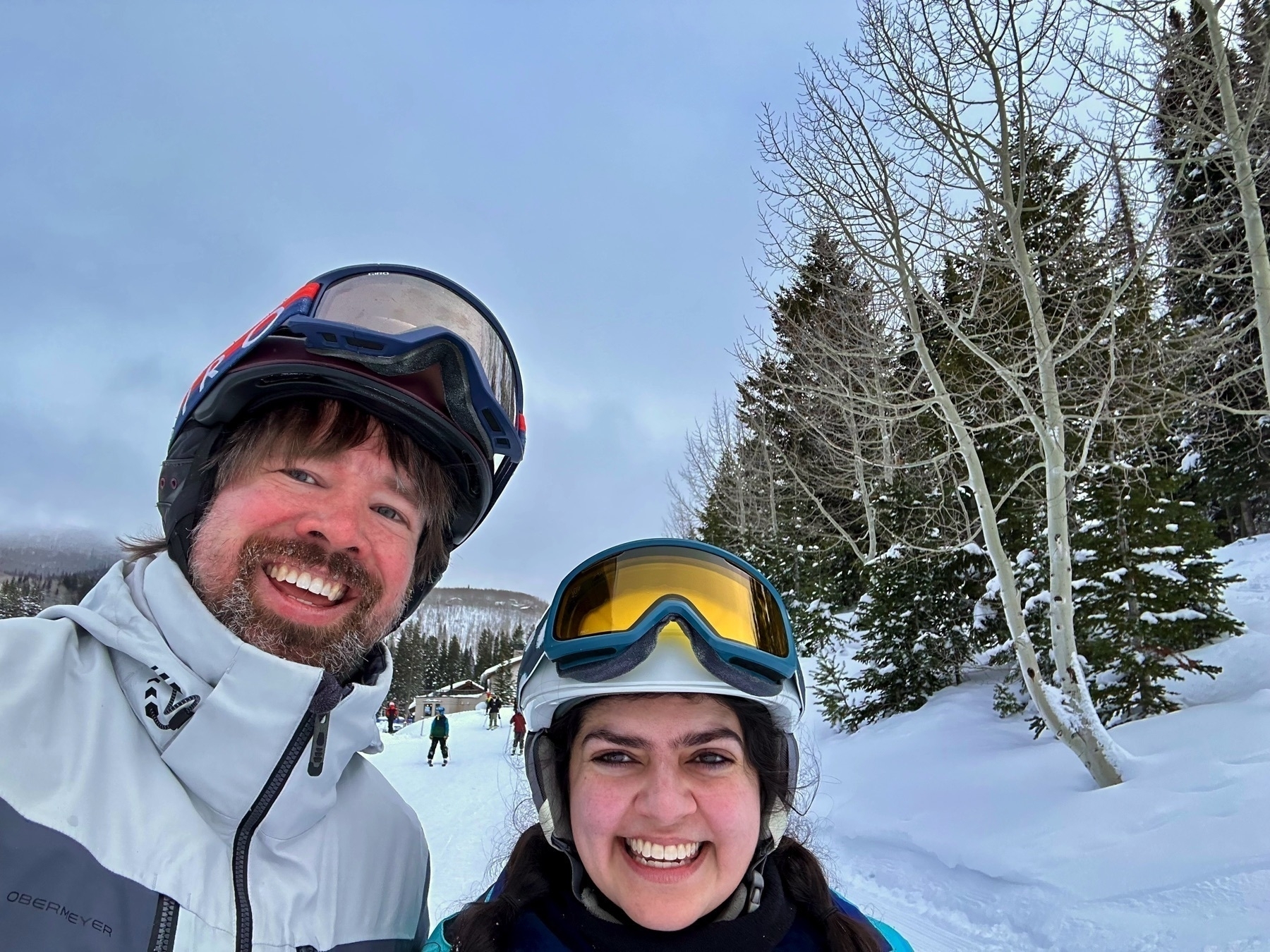 Meera and Jerry in ski jackets and helmets in front of a snowy landscape at Solitude ski resort.