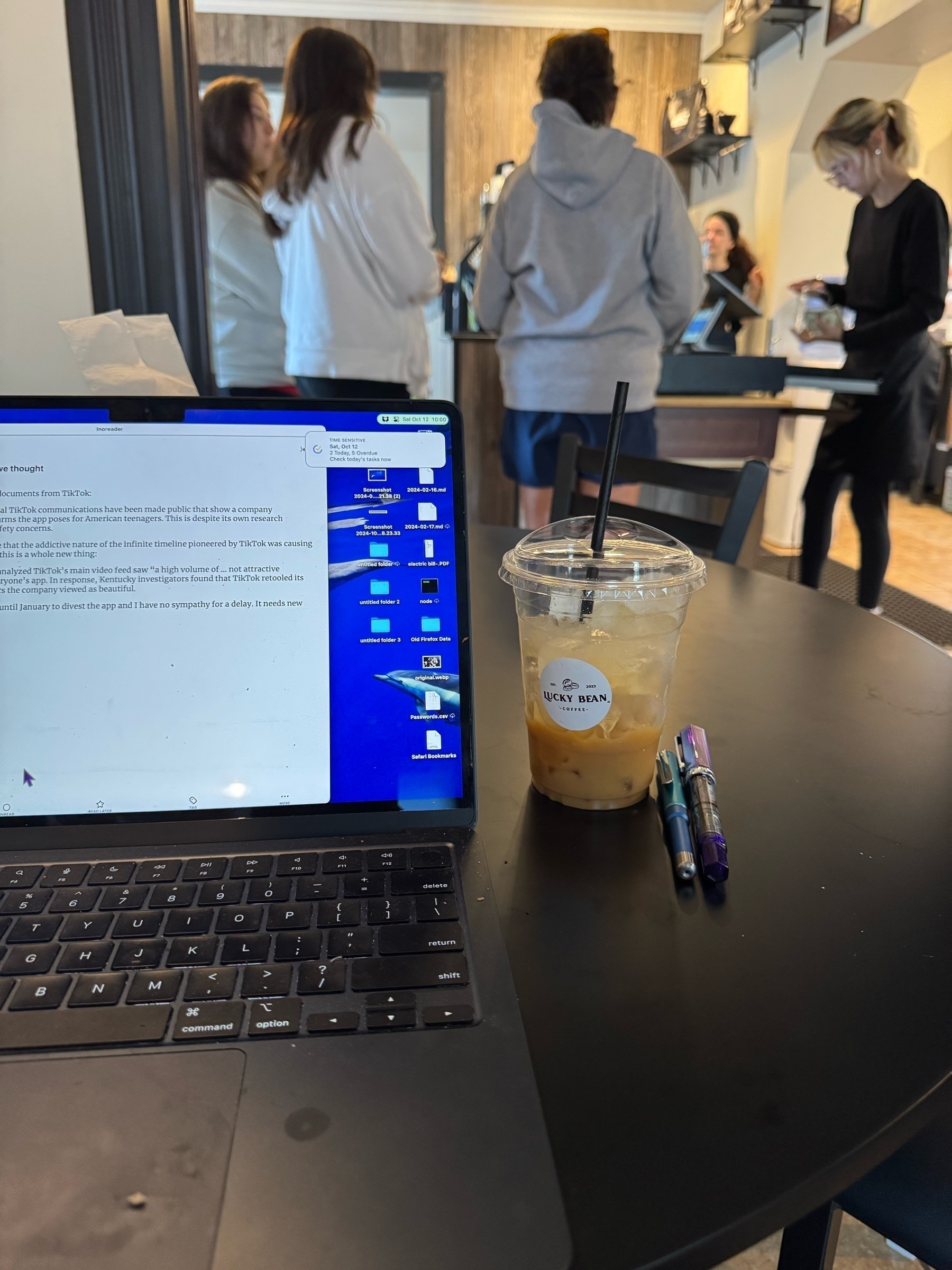 MacBook Air, coffee cup on table. Barista making coffee in background 