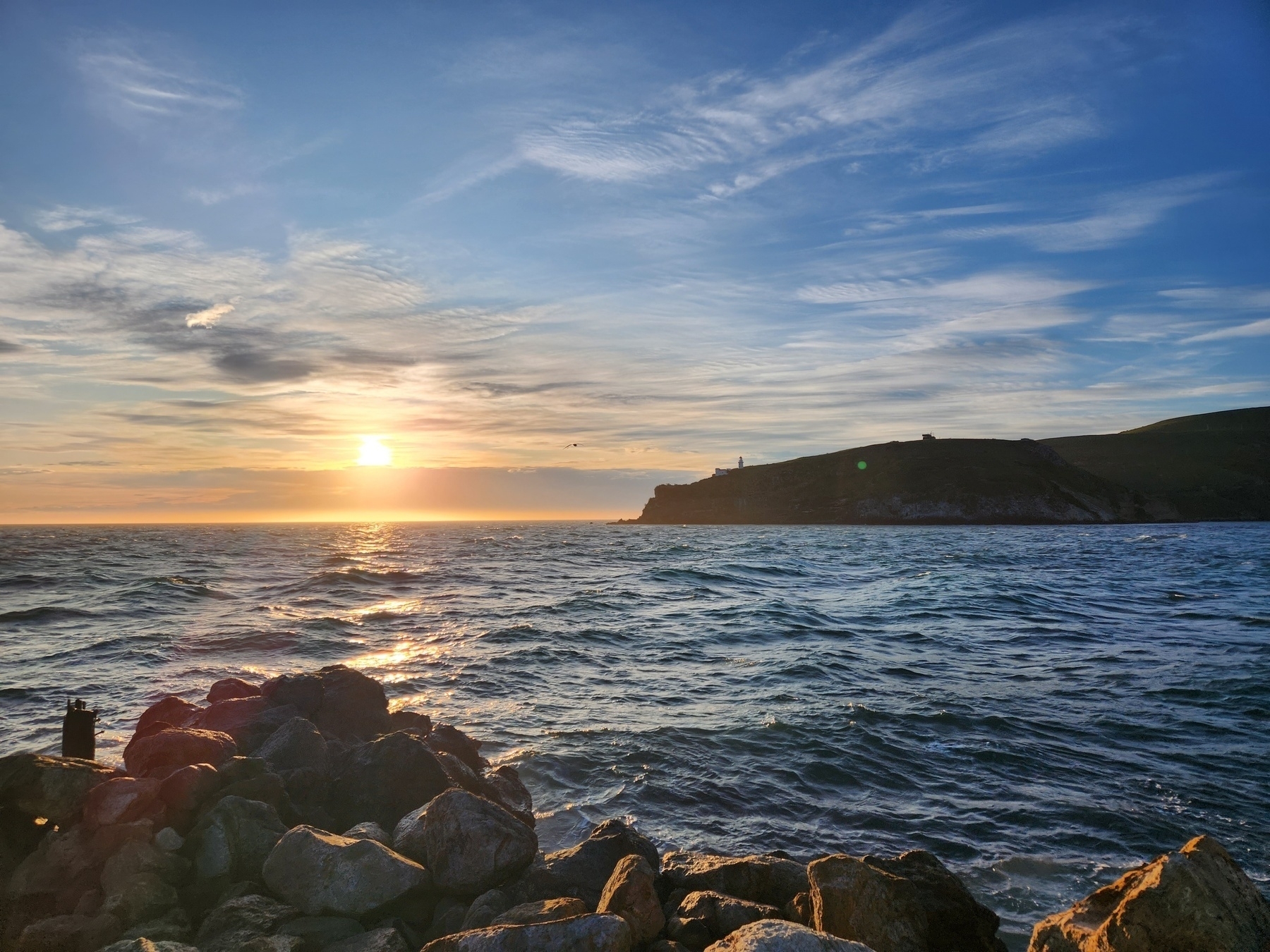 Sunrise to the left of a headland with lighthouse shilloutte