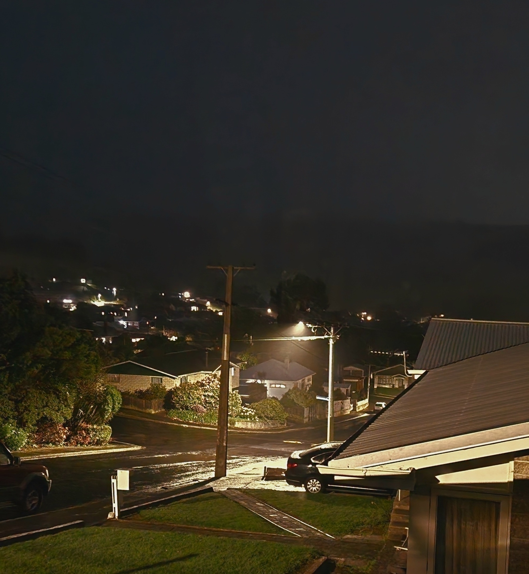 Looking at a streetlight at night that shows light rain drops within the light beam. Edge of house to the right.