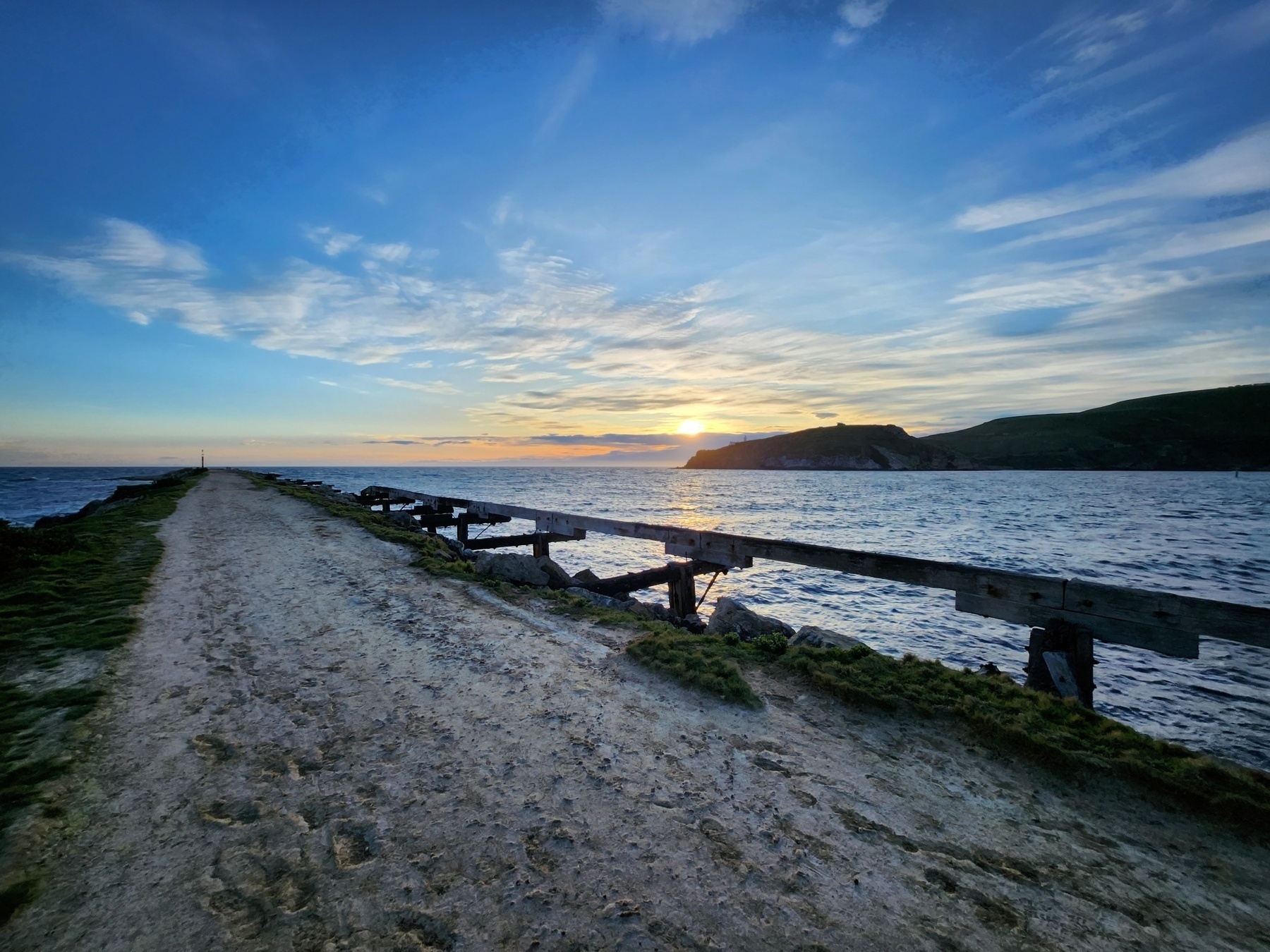 Sunrise over headland with lighthouse shilloutte on the right and looking down a breakwater on the left.