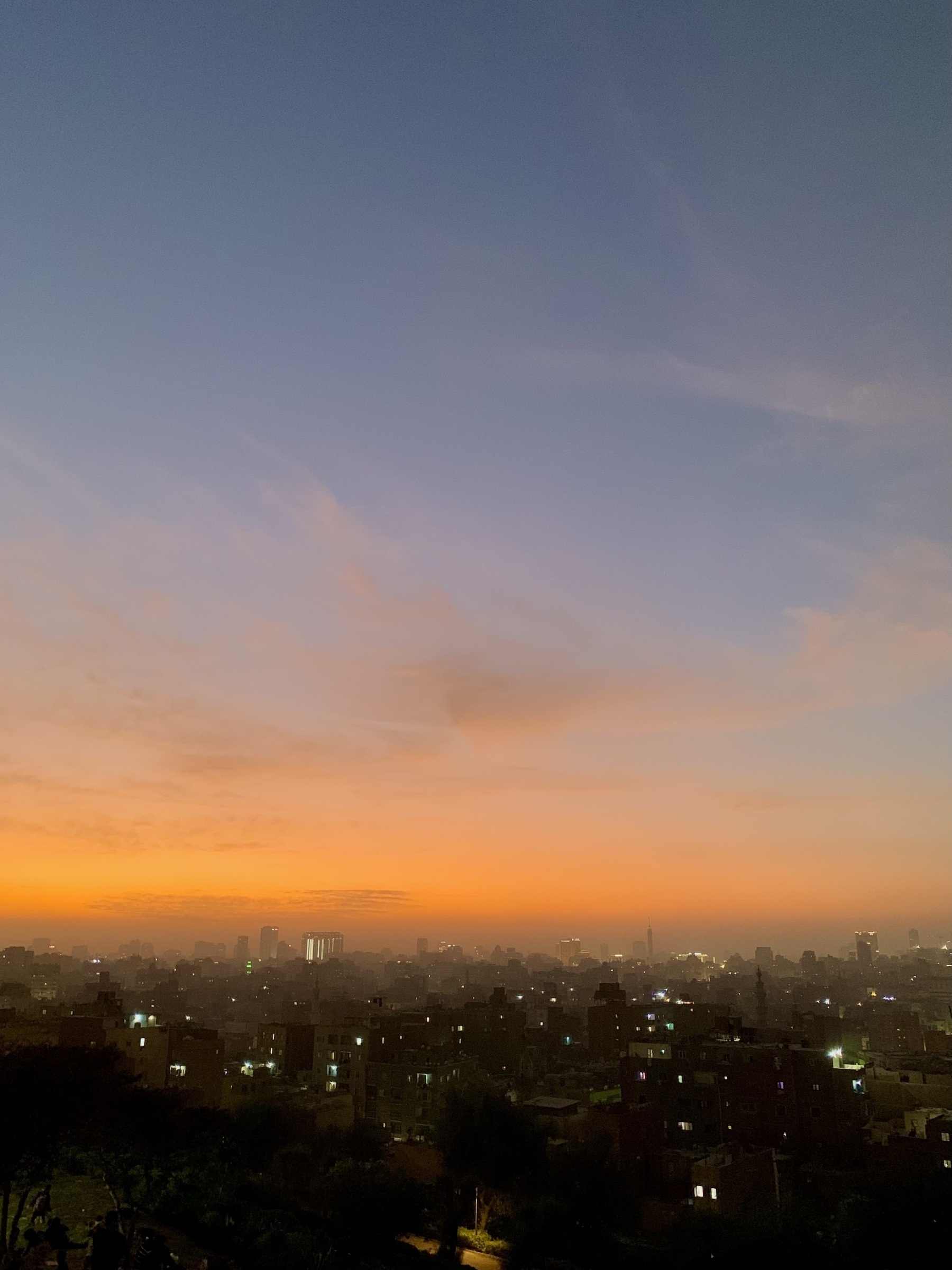 A city skyline at dusk is silhouetted against a vibrant orange and blue sky.