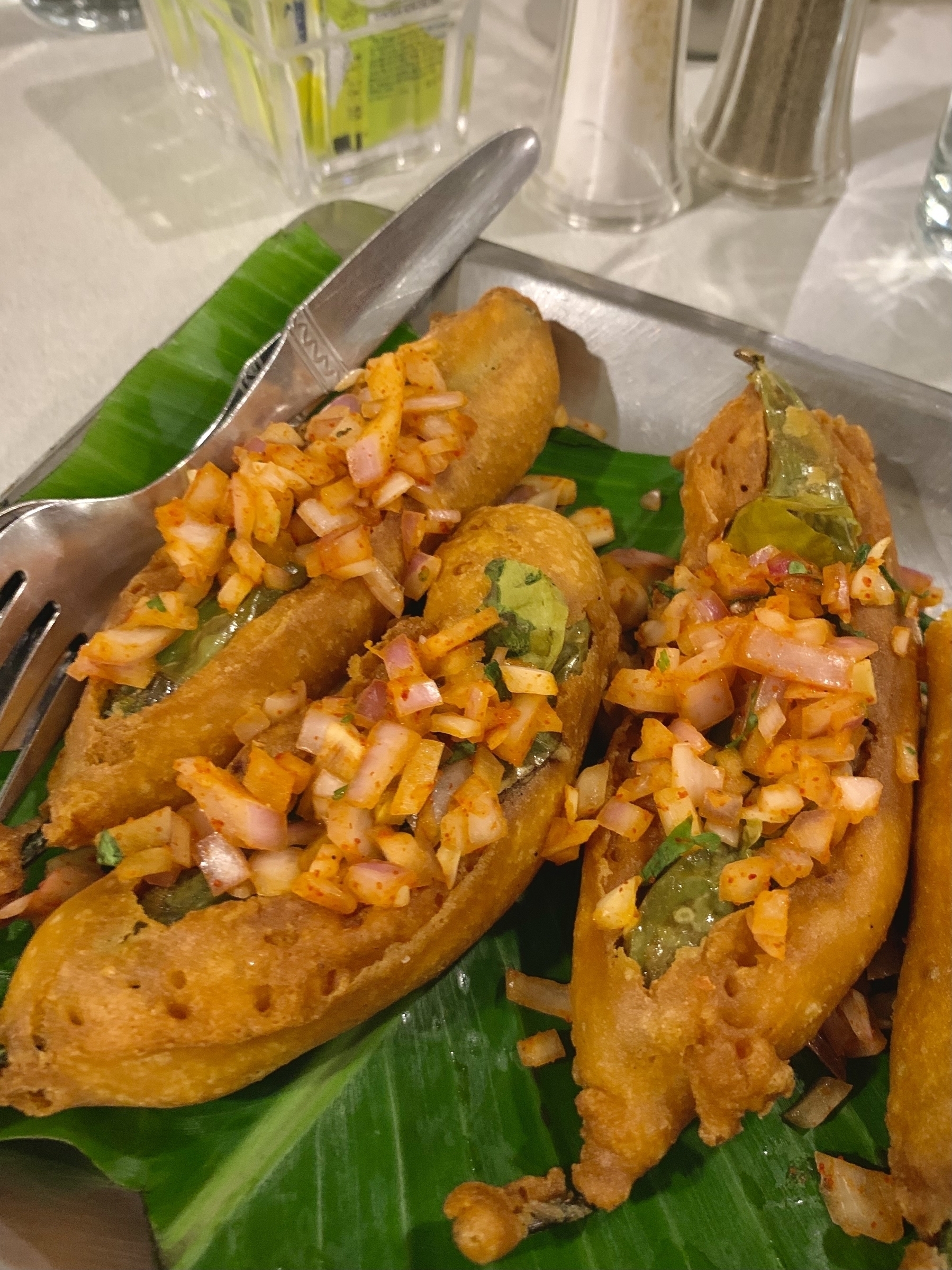 Deep-fried chili bajji stuffed with a spicy filling and topped with diced onions and seasoning are served on a banana leaf.