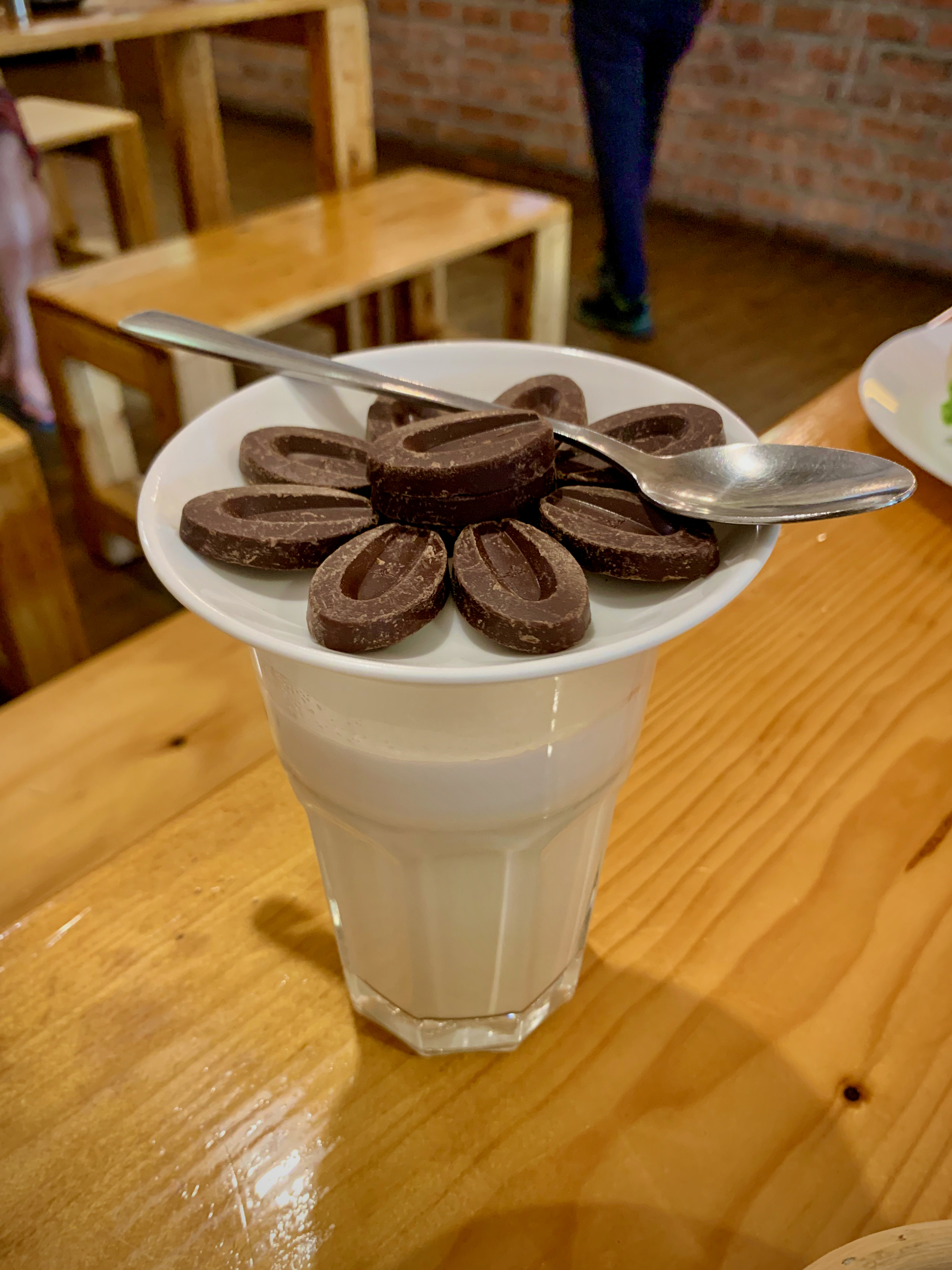 A glass of frothed milk, with coins of dark chocolates in a quarter plate