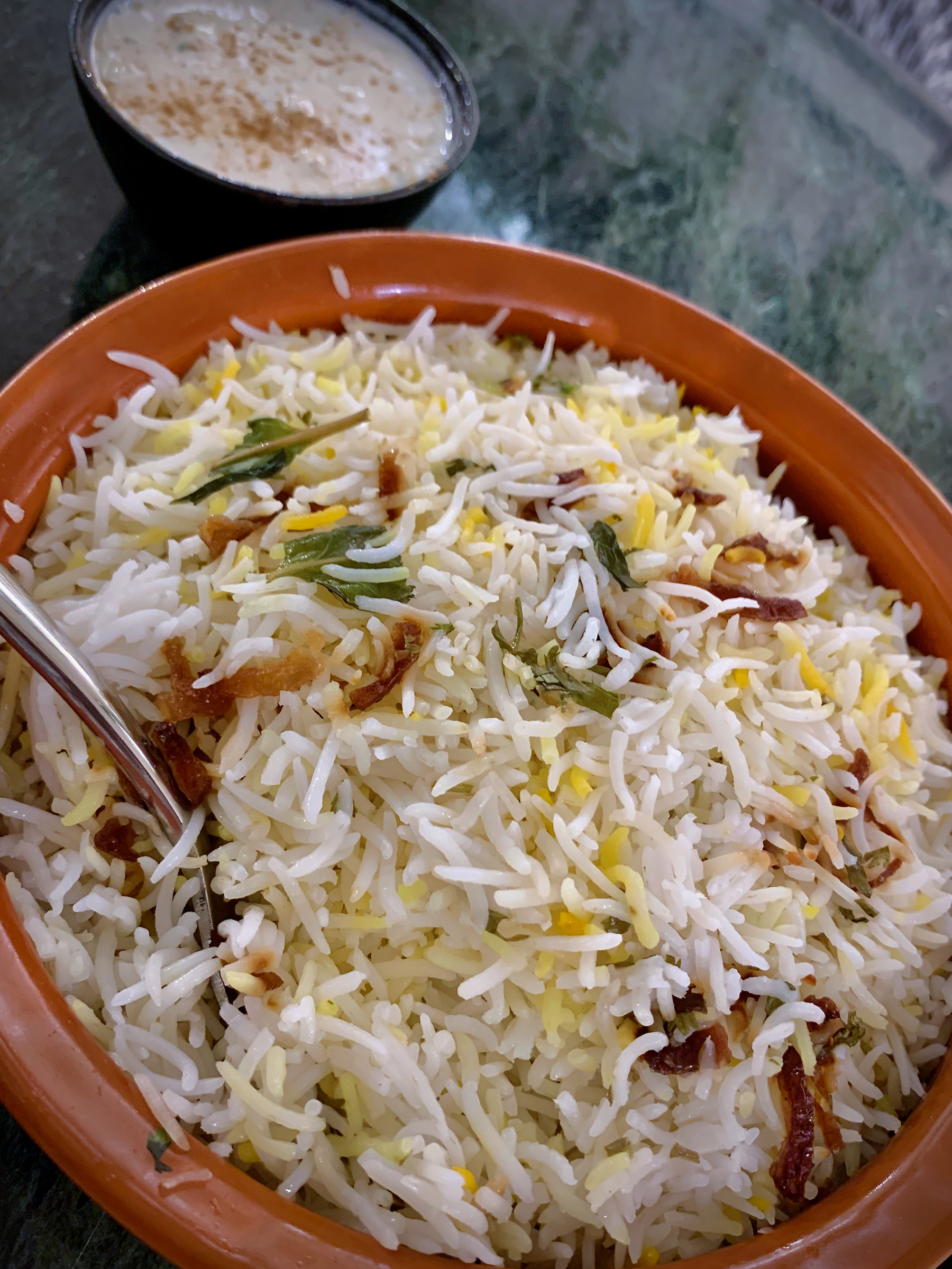 A bowl of lamb dum biryani served with yoghurt raita.