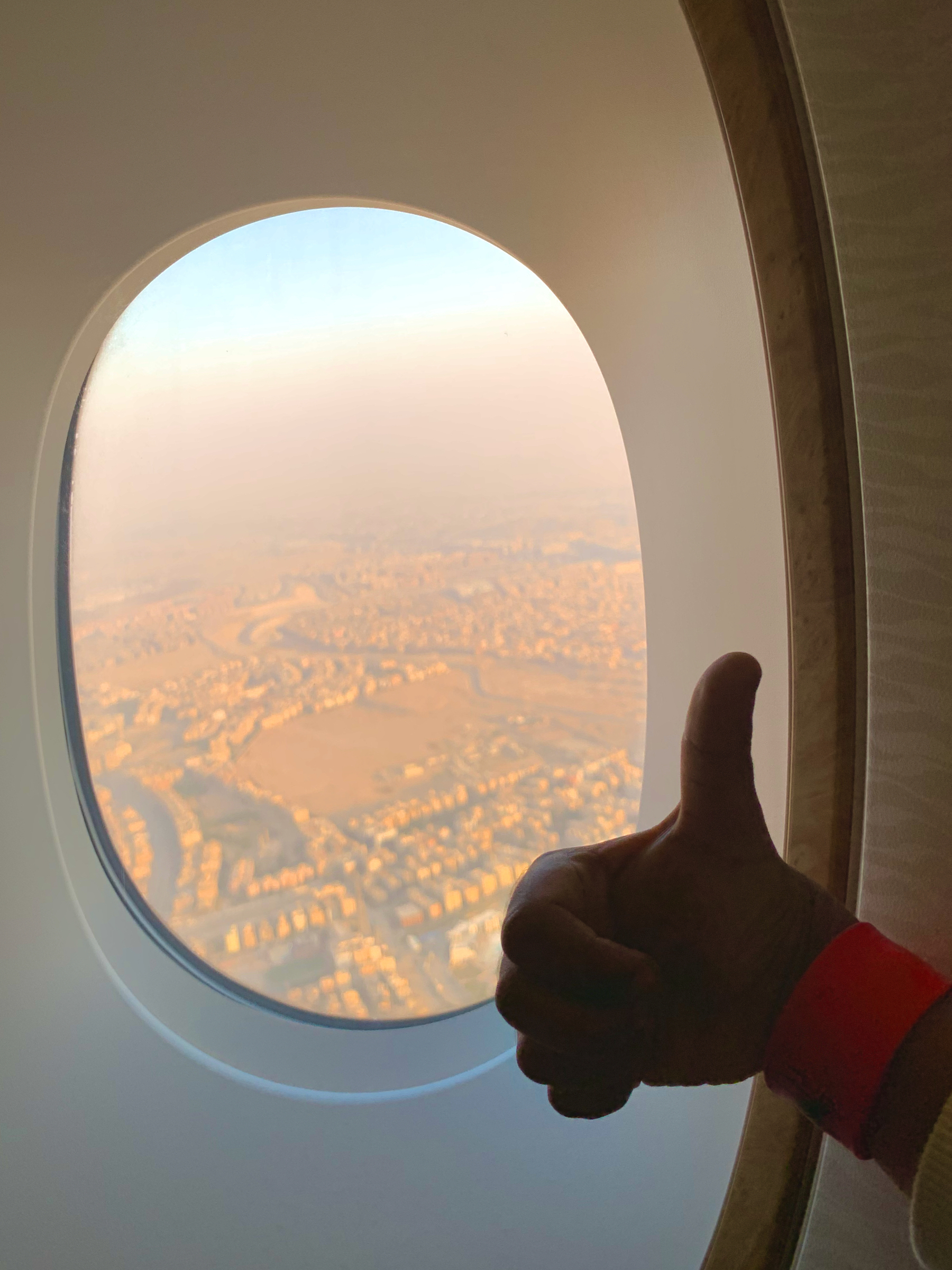 A view of a sandy cityscape of Cairo from an airplane window with a boy's hand showing a thumbs-up gesture.