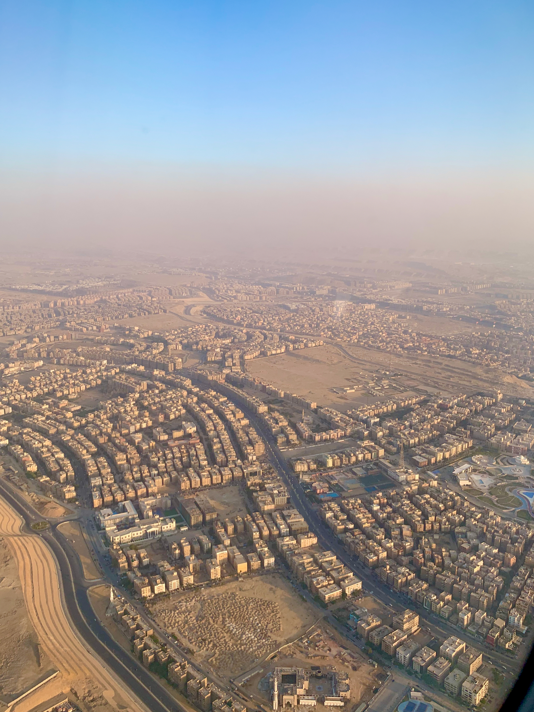 Aerial view of a sprawling cityscape of Cairo with densely packed buildings and winding roads under a clear blue sky.