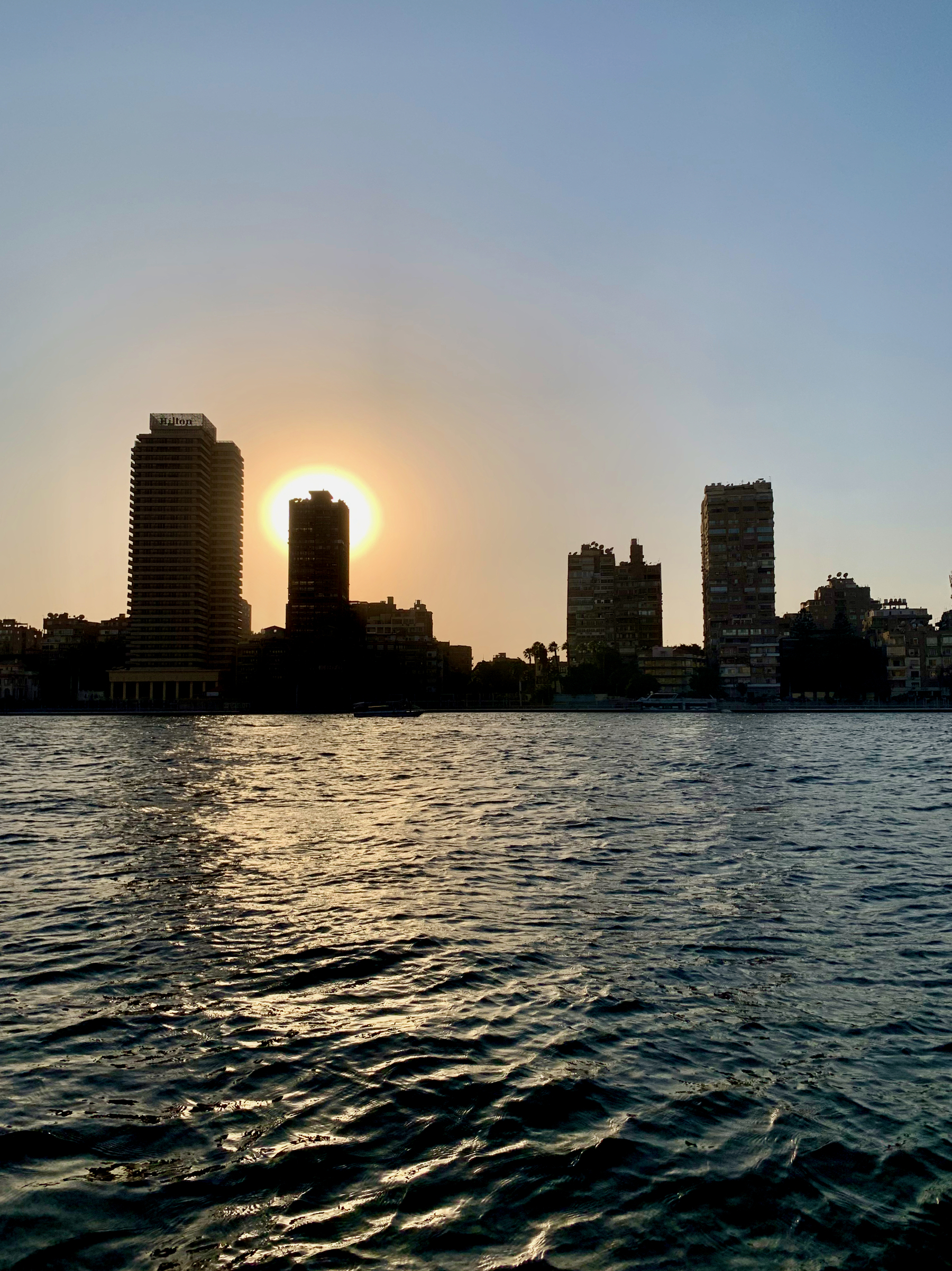 Auto-generated description: A sunset view over a river with silhouetted city buildings in the background.