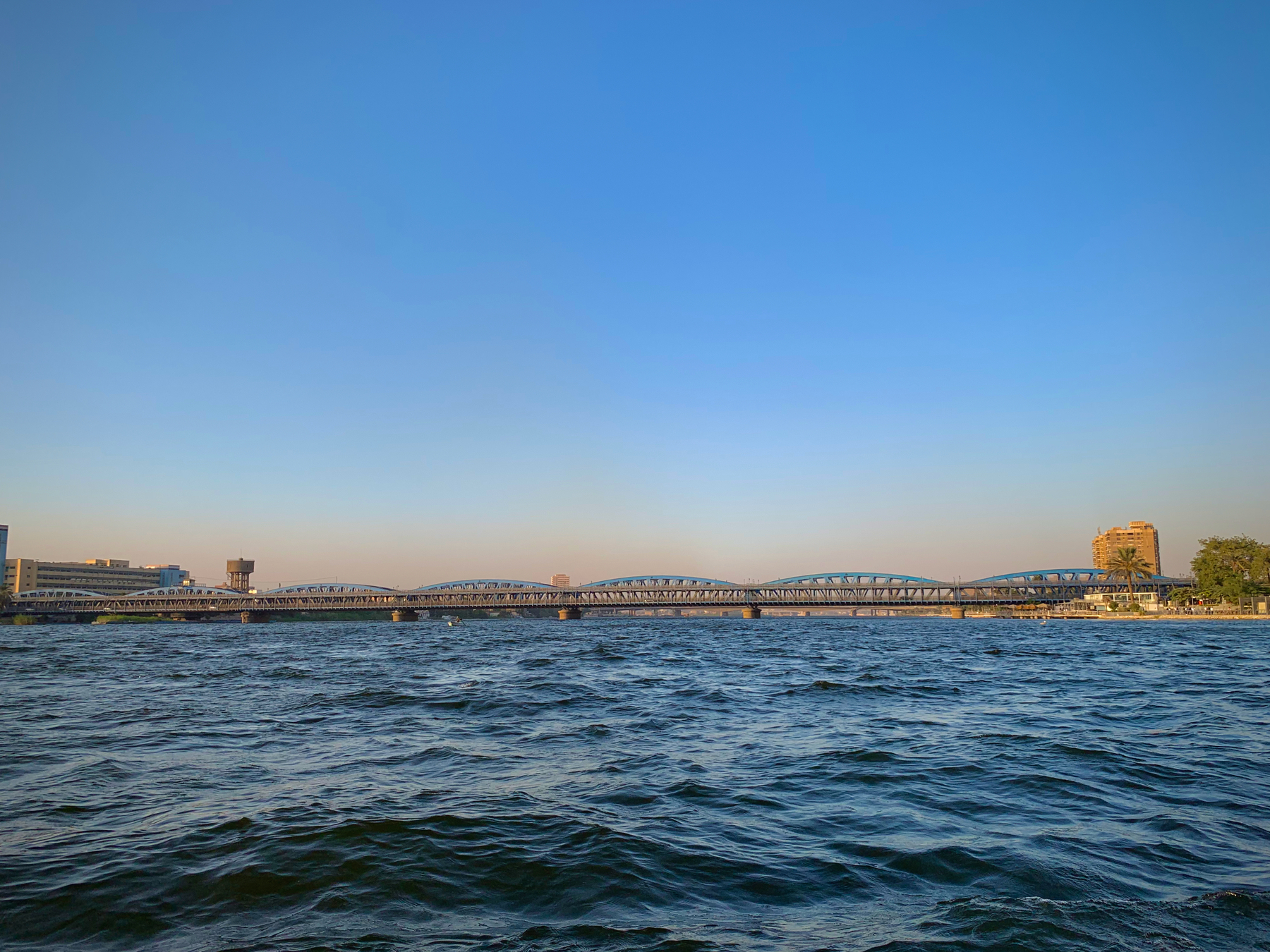 Auto-generated description: A large bridge spans over a wide river under a clear blue sky.