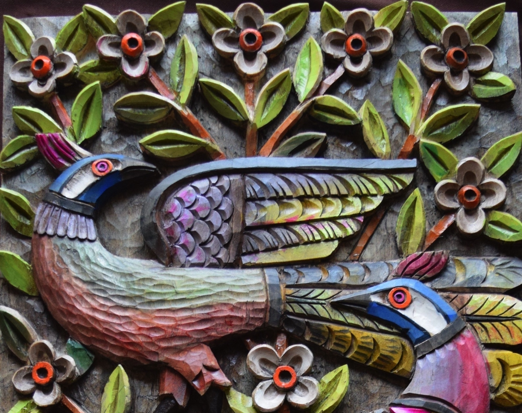 Detail of relief wood carving of birds against foliage, painted in bright blues, oranges, and greens.