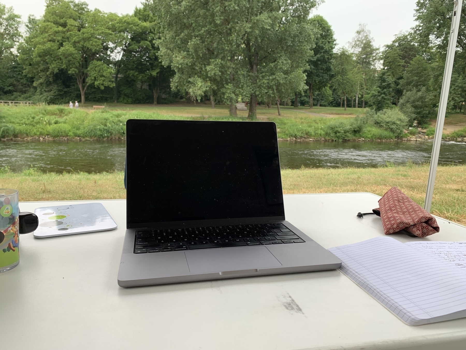 Laptop computer and notebook on table with river and park with trees in background