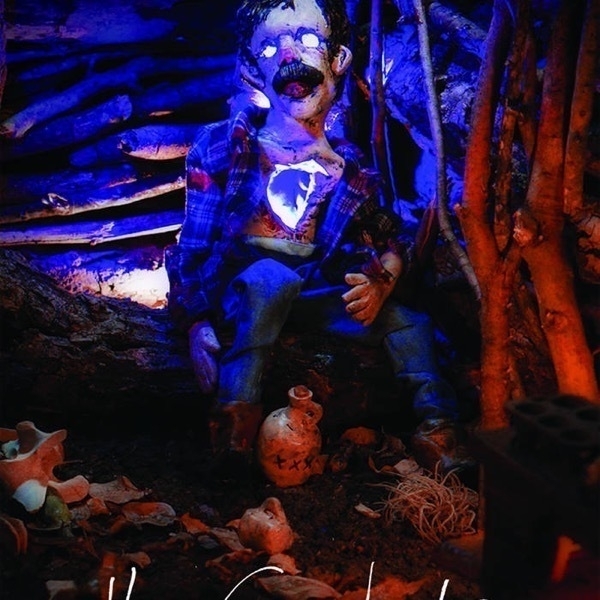 A doll with a heavy mustache and whited out eyes wearing a checkered shirt and blue pants sits among pottery shards and logs in a creepy, high-contrast red and blue lighting.
