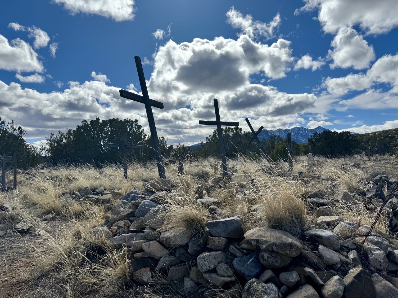Rocks piled on graves in foreground with wooden crosses slanting and a bright blue sky with white clouds in background