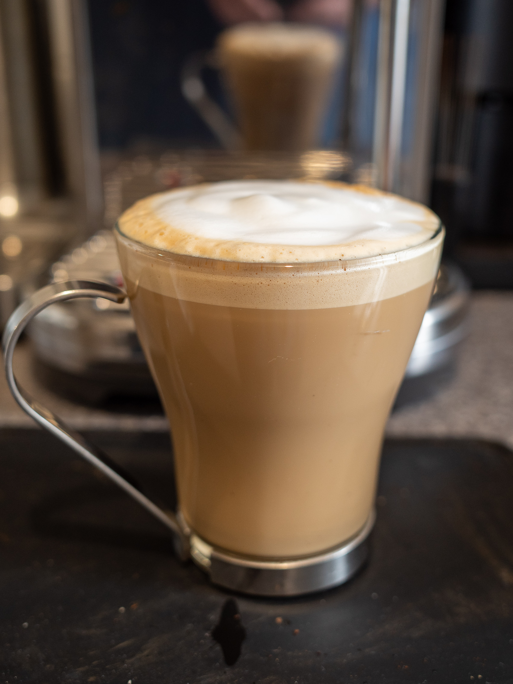 A flat white coffee in a glass mug.