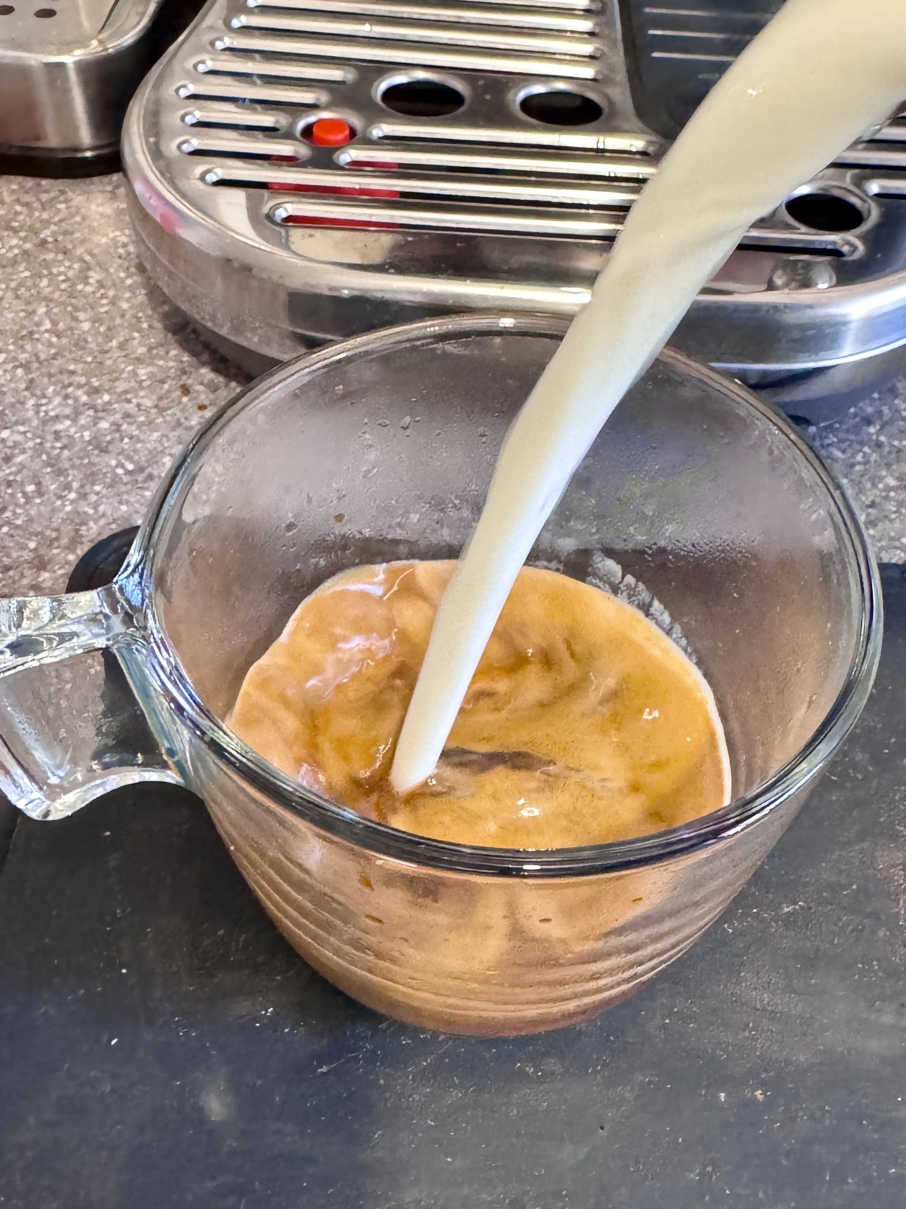 Pouring milk into espresso coffee in a glass mug.