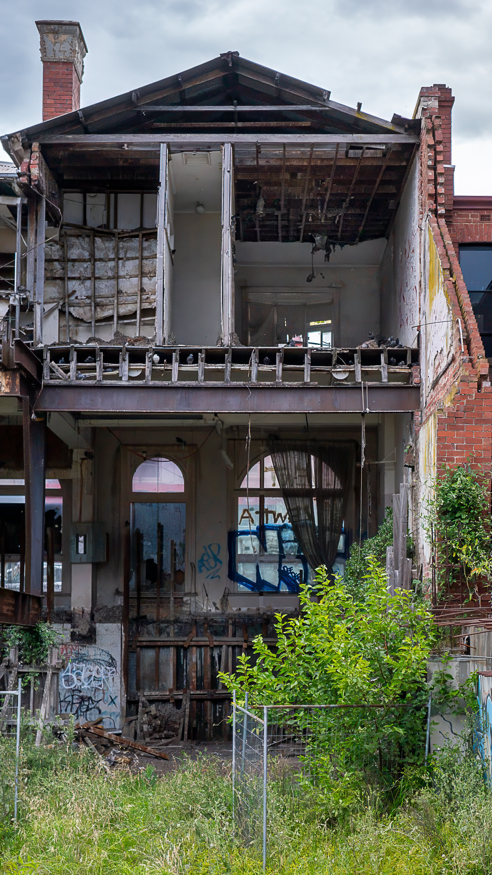 The back of a building that has been partially torn down leaving the front facade and a couple internal walls.