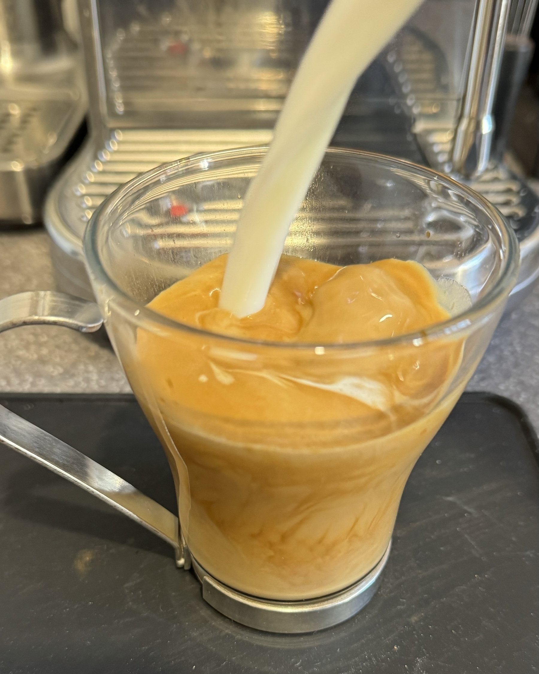 Pouring milk into espresso coffee in a glass mug.