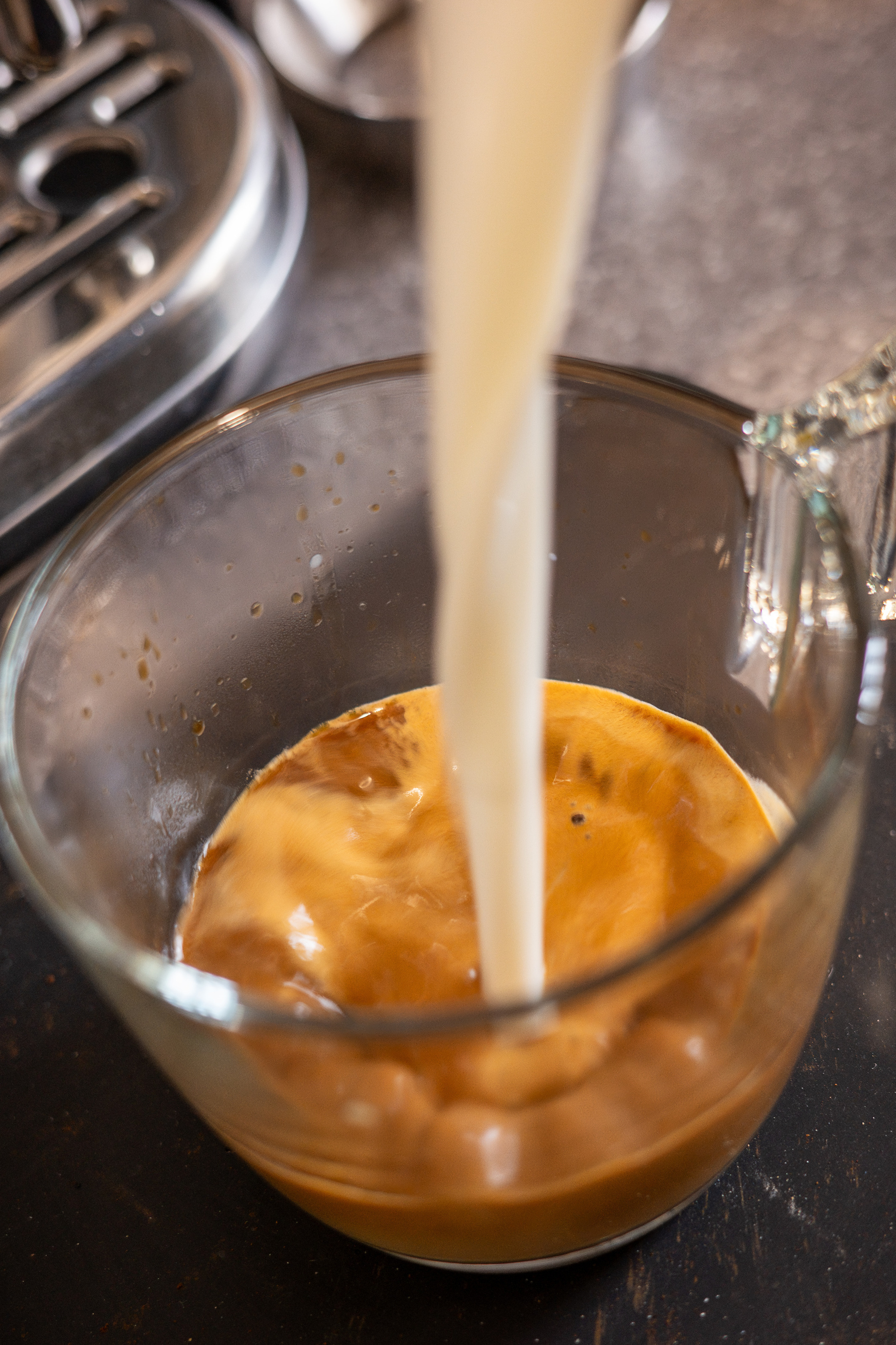 Pouring milk into coffee in a glass mug.