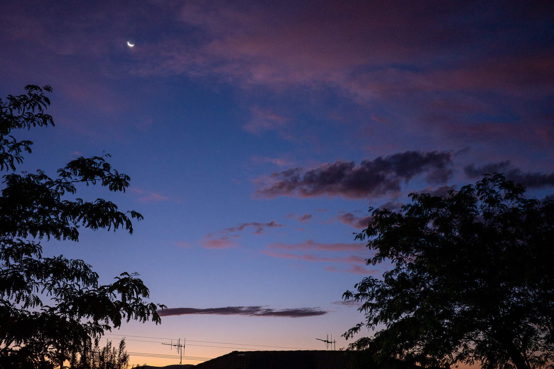 Dark blue sky after sunset. Fain orange glow on the horizon. The moon is visible top left.