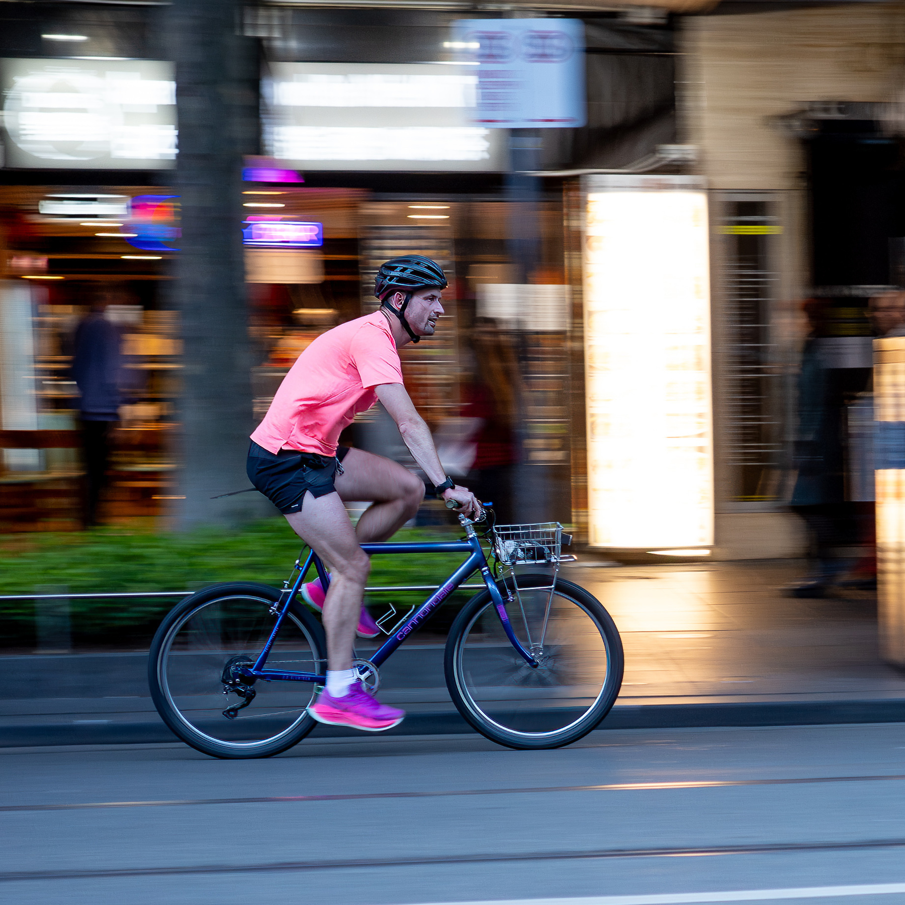 A rider on a flatbar bike, wearing pink / appricot coloured t-shirt and running shoes